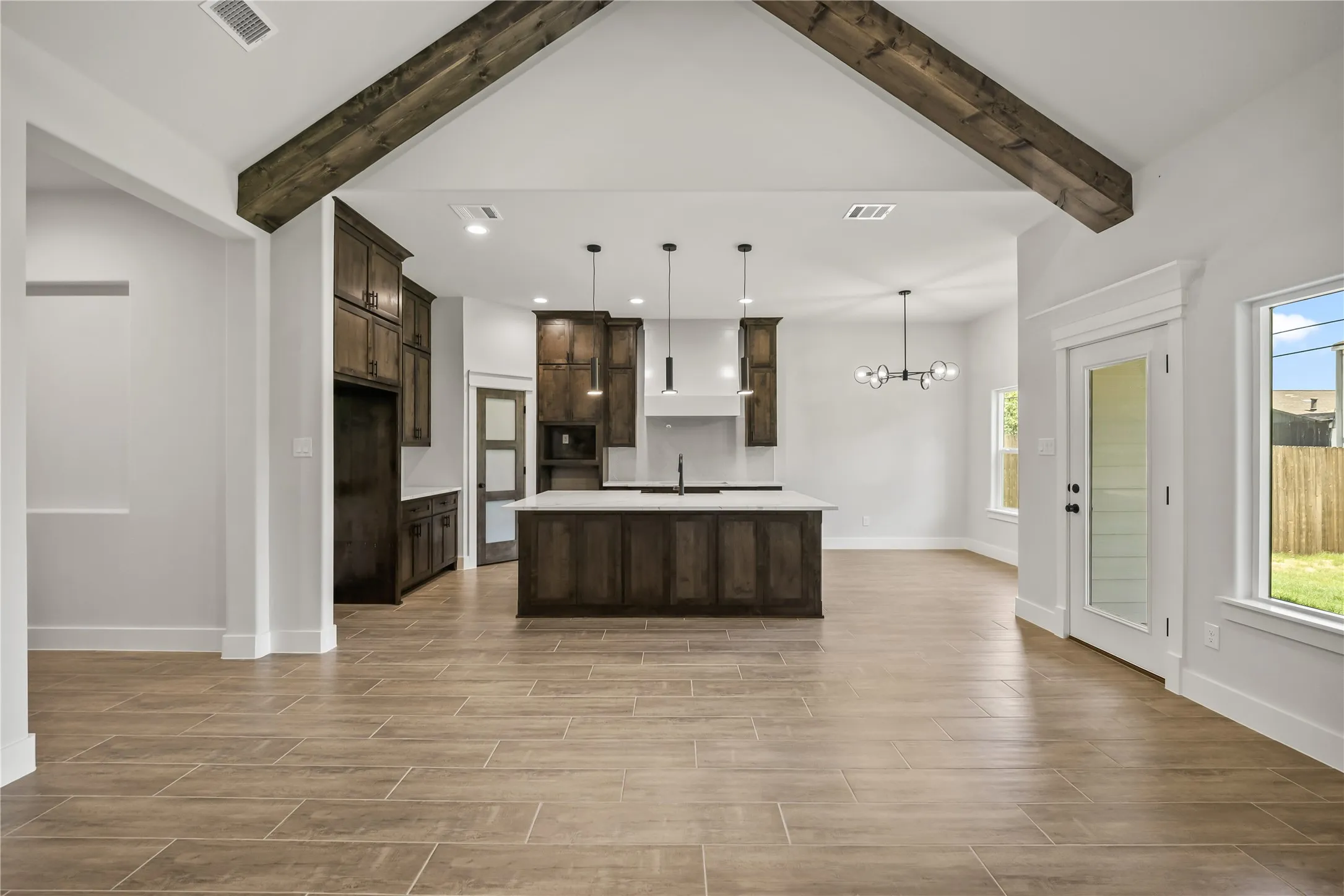 Open concept living space featuring a kitchen island with seating, vaulted ceiling with exposed wood beams, wood-look tile flooring, shaker-style cabinetry, and a glass-paneled exterior door