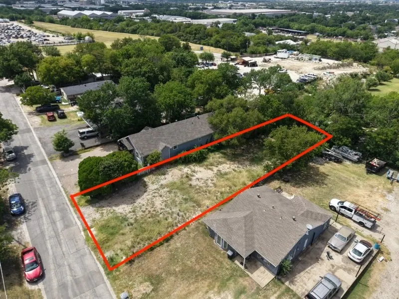 Vacant lot outlined in red, featuring natural vegetation and mature trees, with street frontage