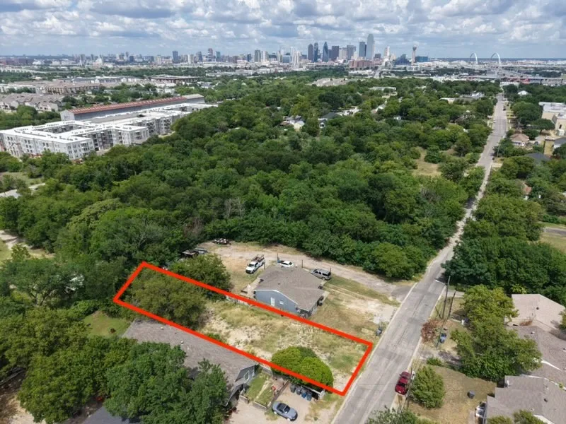 Expansive land parcel featuring existing structures, a partially cleared lot, and mature trees, with a clear view of the distant city skyline