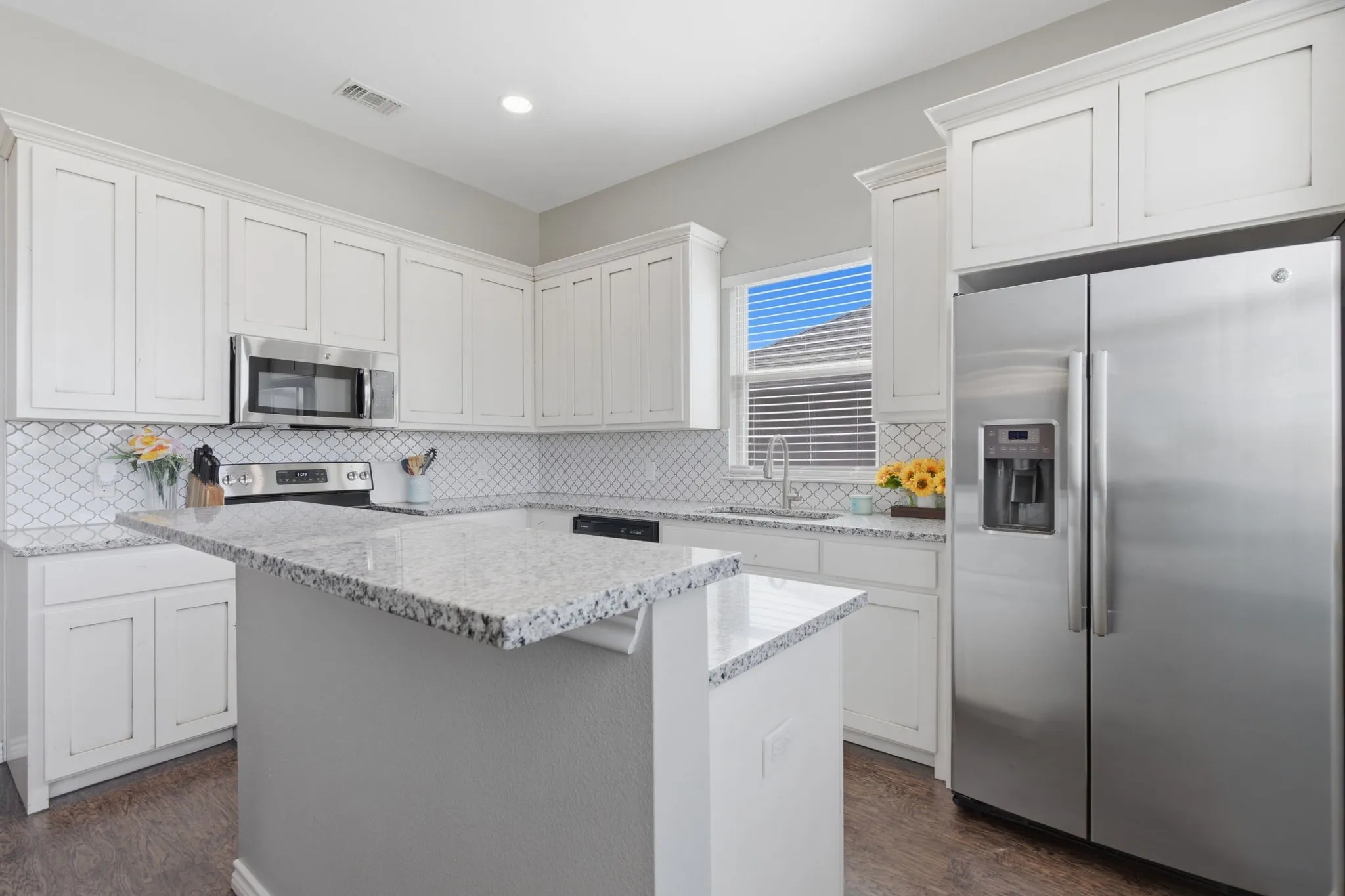 Kitchen with stainless steel appliances, white cabinetry, a center island, and light stone counters