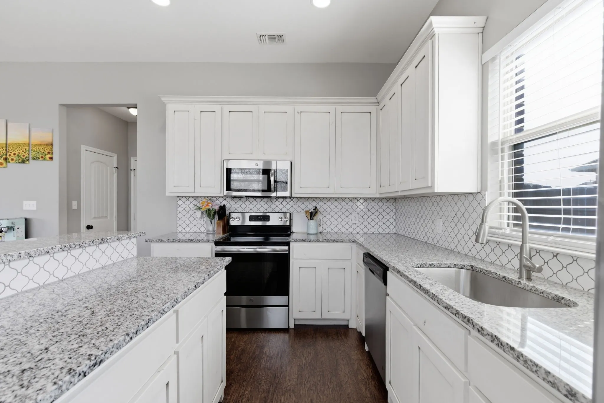 Kitchen with stainless steel appliances, light stone countertops, white cabinets, dark wood-type flooring, and recessed lighting