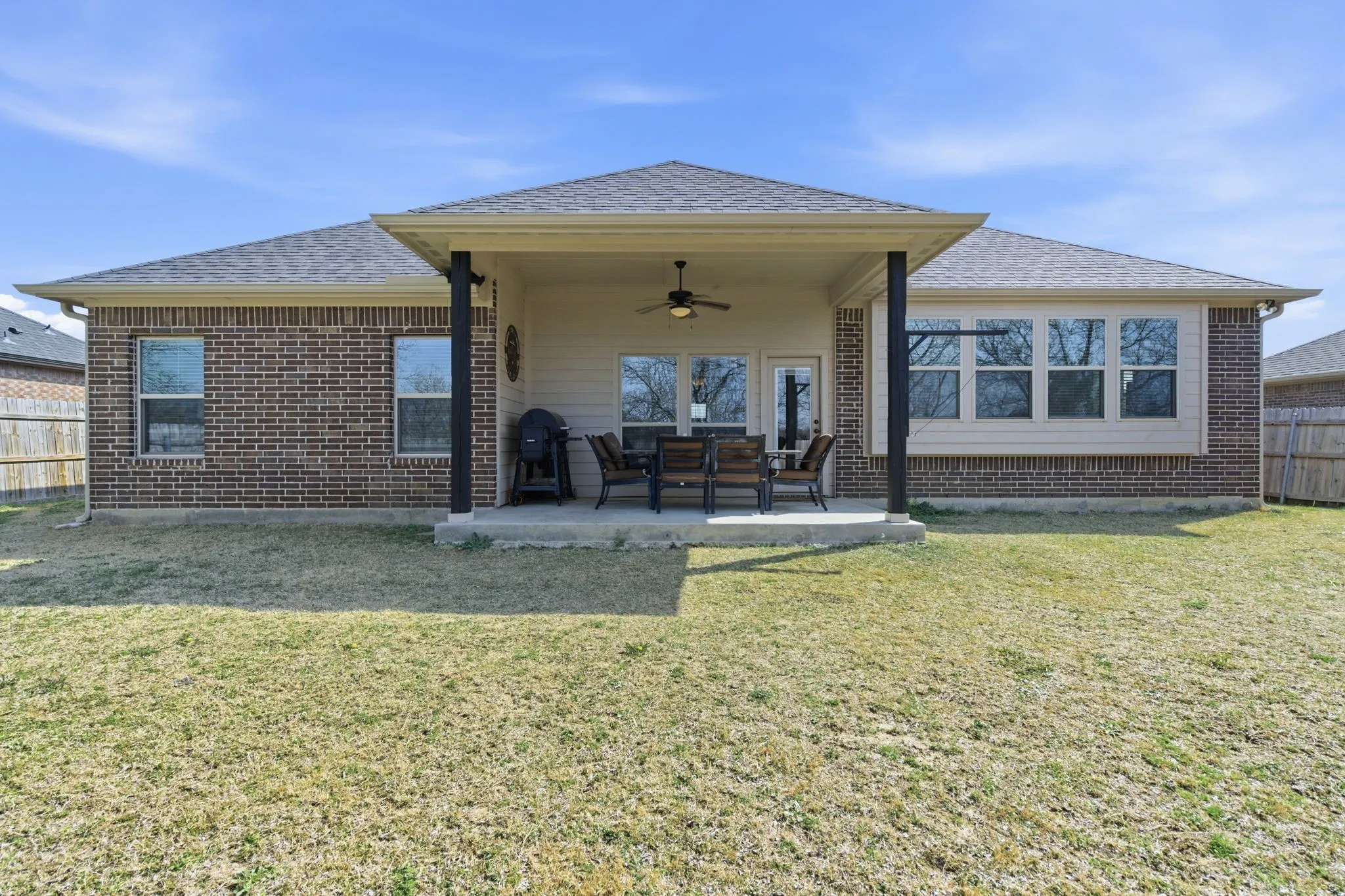 Back of property with ceiling fan, a patio area, a shingled roof, and brick siding