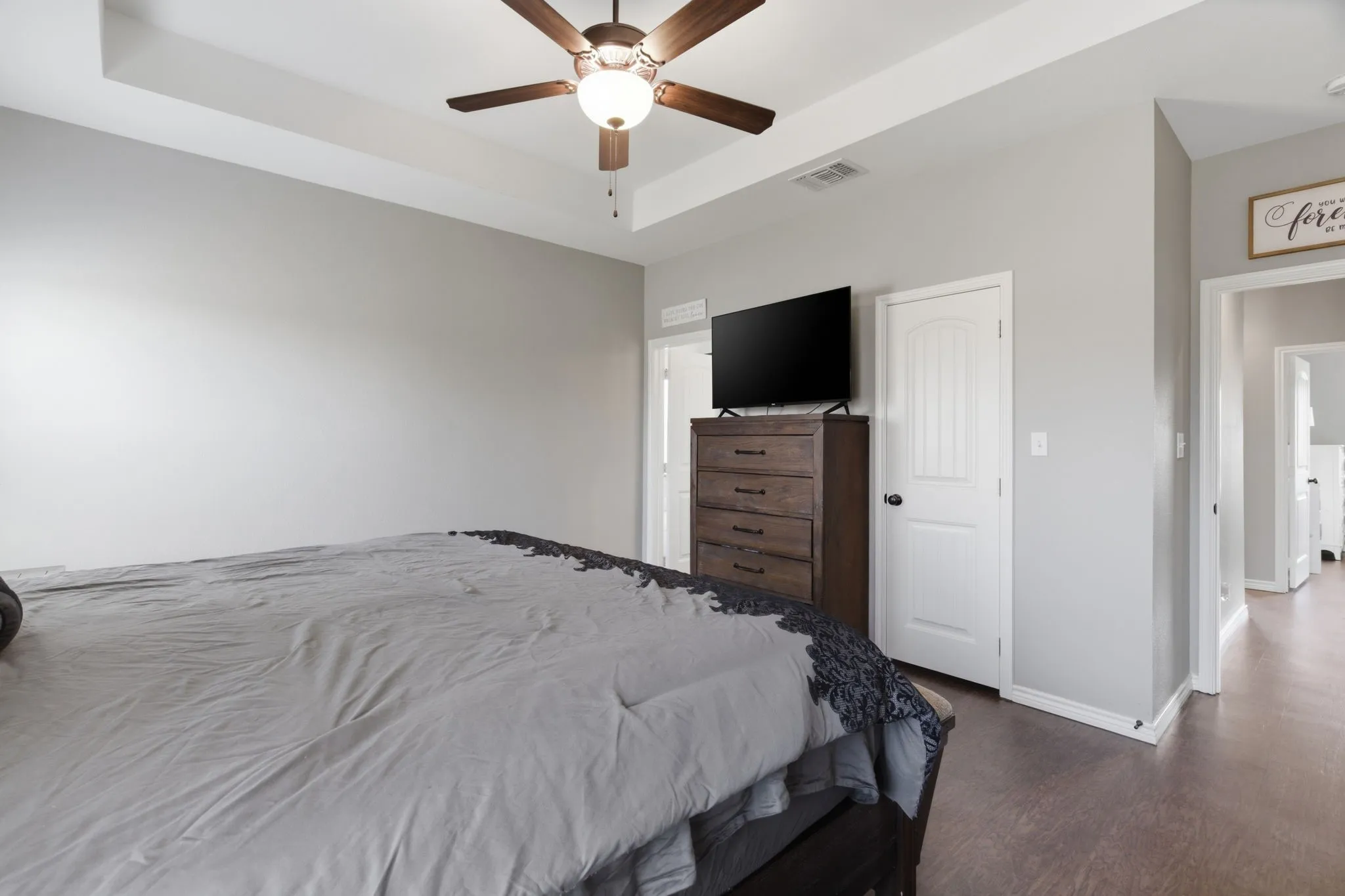 Bedroom with a raised ceiling, ceiling fan, dark wood-type flooring, and a closet