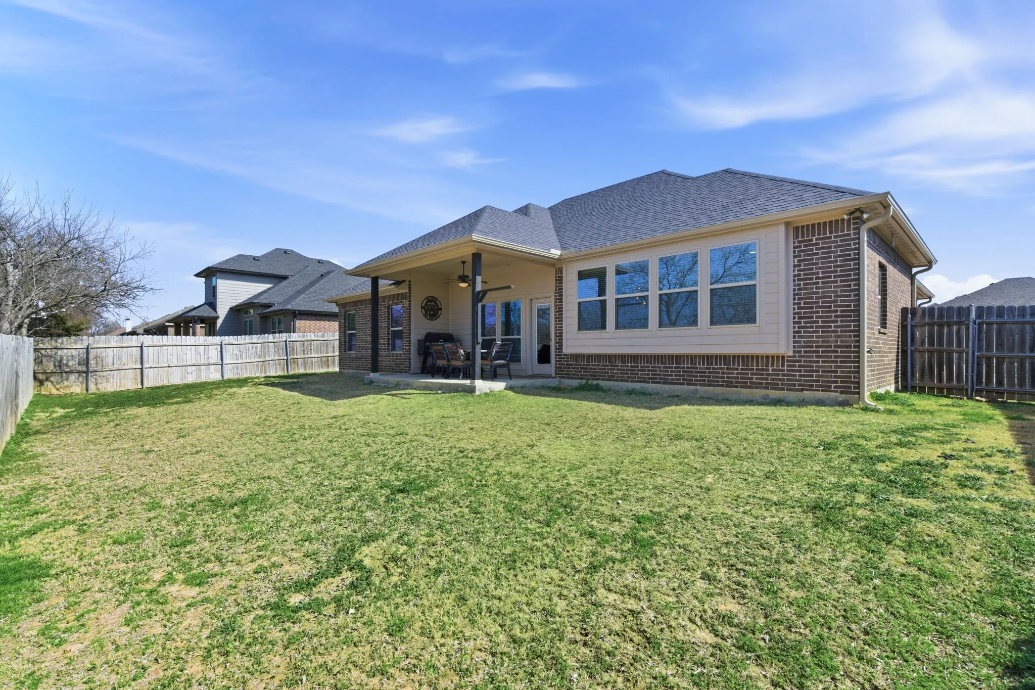 Rear view of house with ceiling fan, brick siding, a fenced backyard, a patio area, and roof with shingles