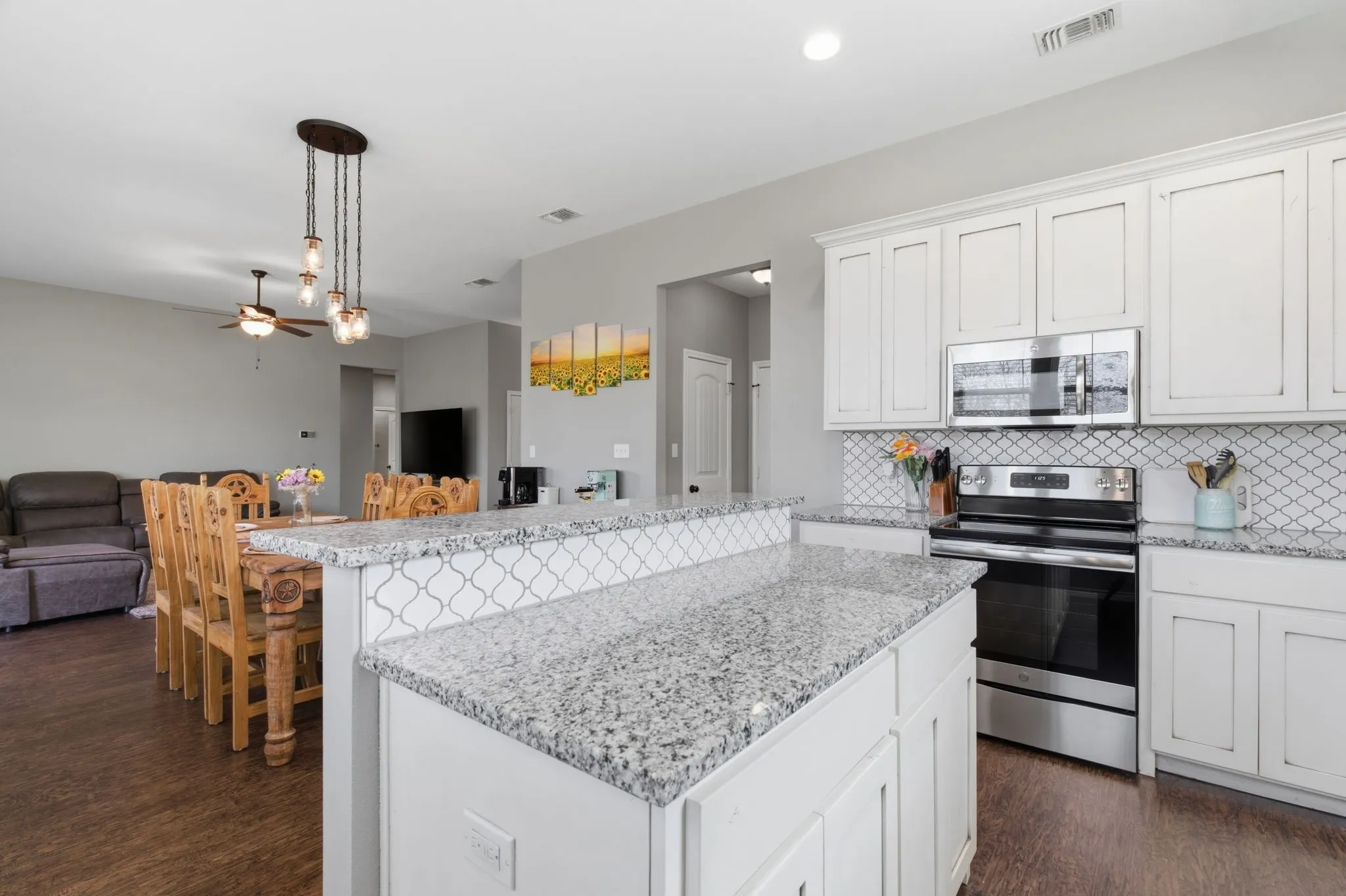 Kitchen with stainless steel appliances, white cabinets, ceiling fan, decorative light fixtures, and light stone countertops