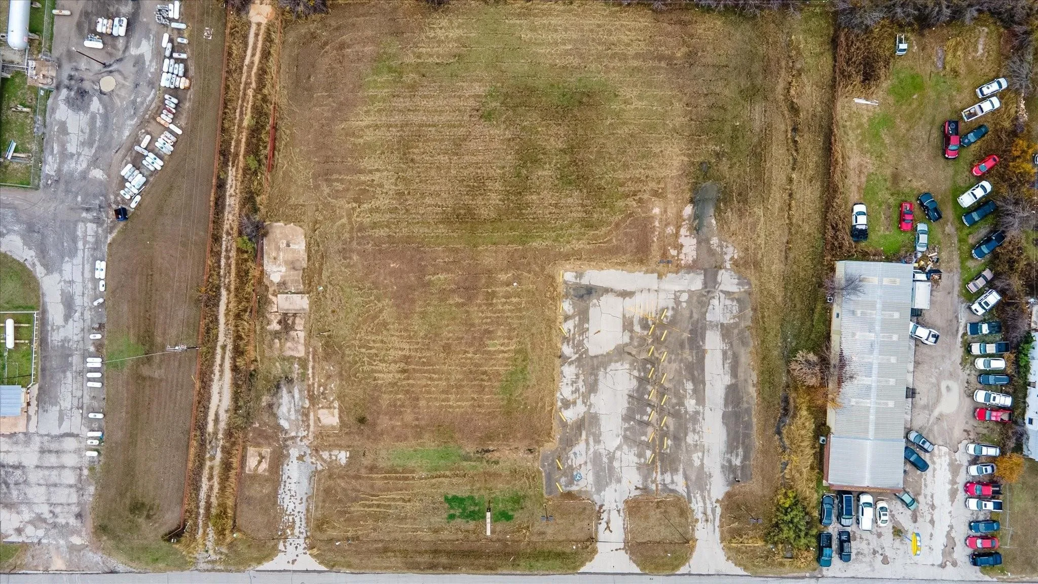 Expansive land parcel featuring a large grassy area, concrete pads, and adjacent structures