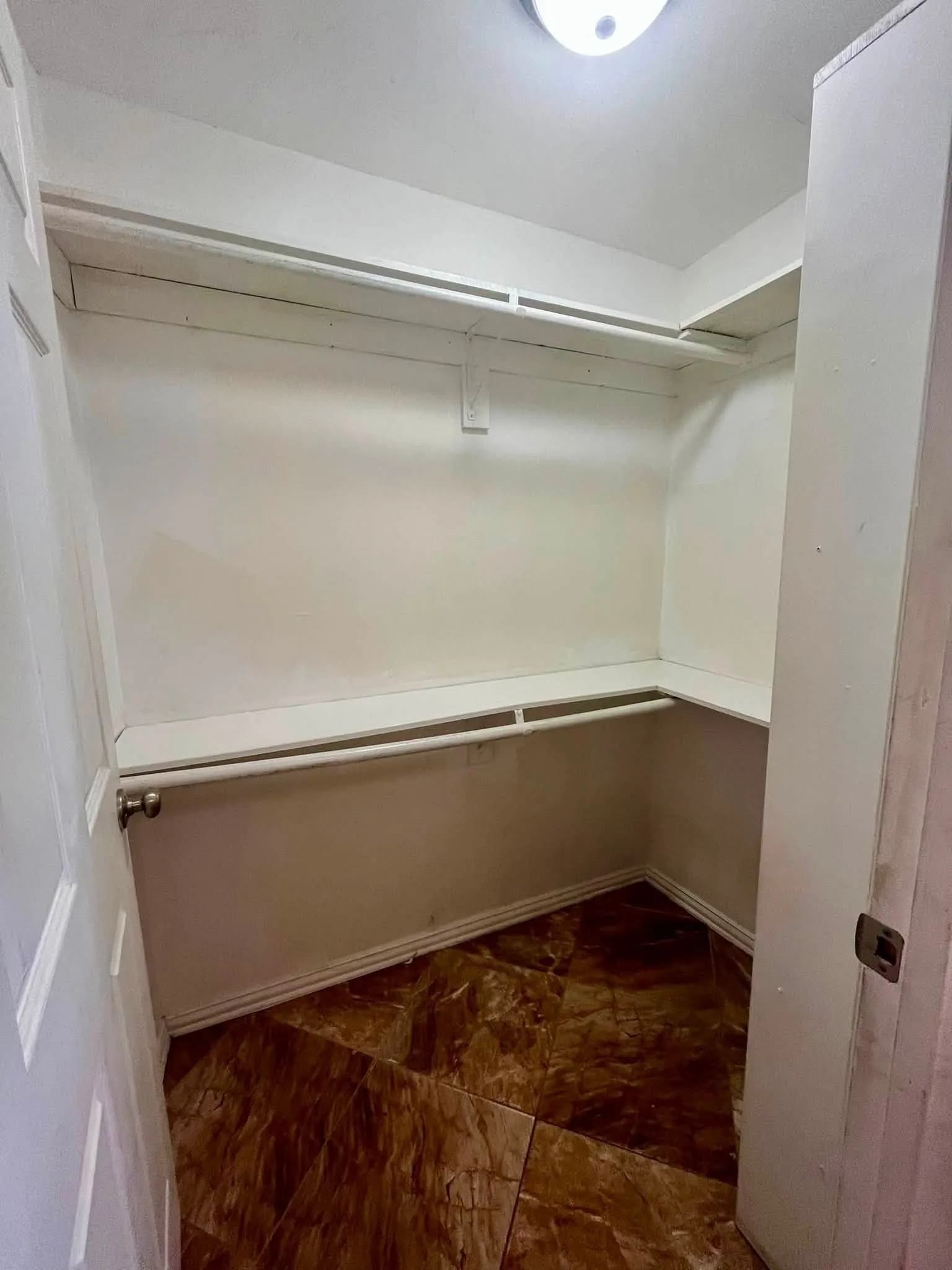 Walk-in closet with brown patterned tile flooring, white walls, built-in shelving, and hanging rods