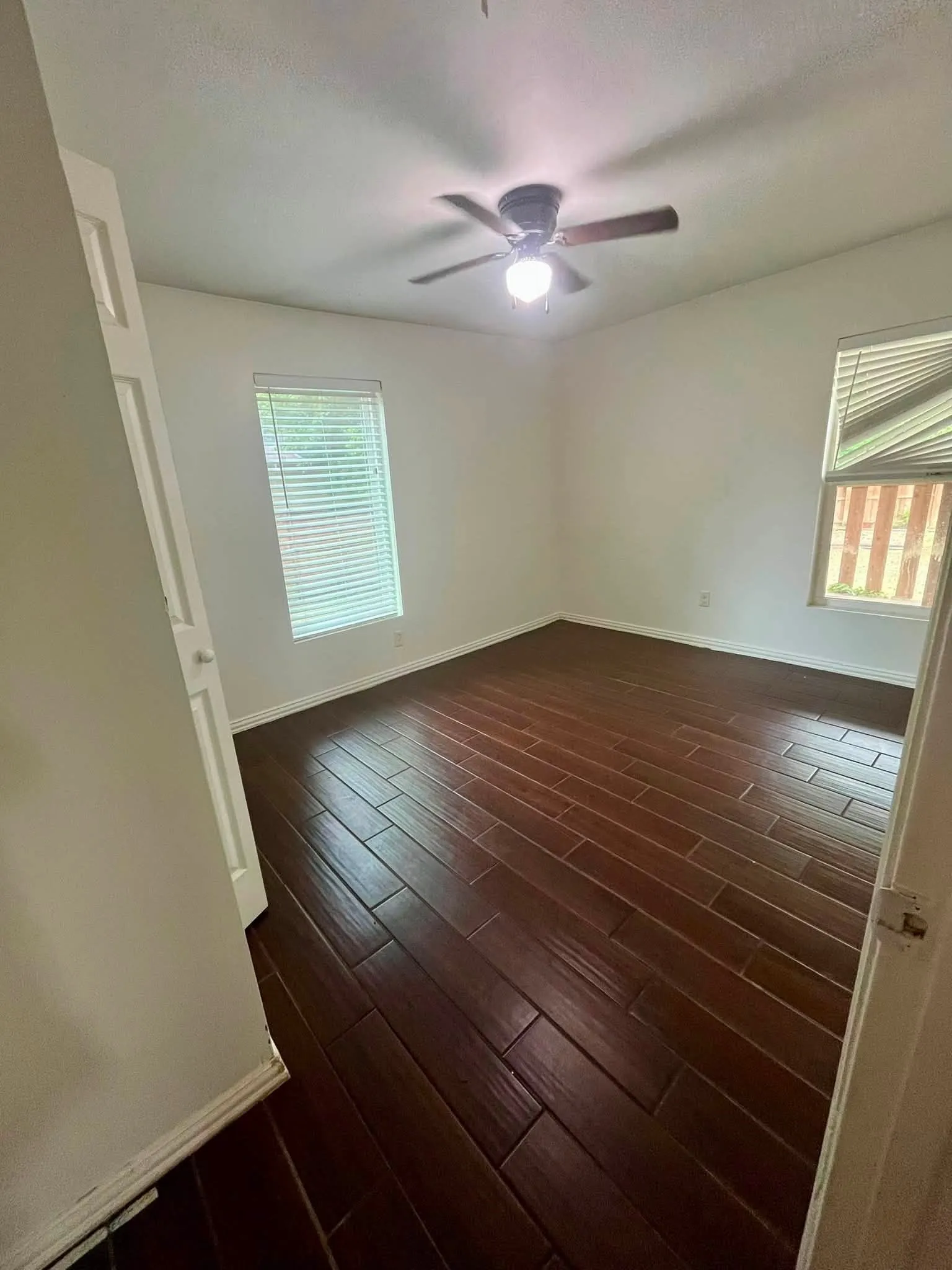 Room featuring dark wood-finish flooring, white walls, and two windows with horizontal blinds