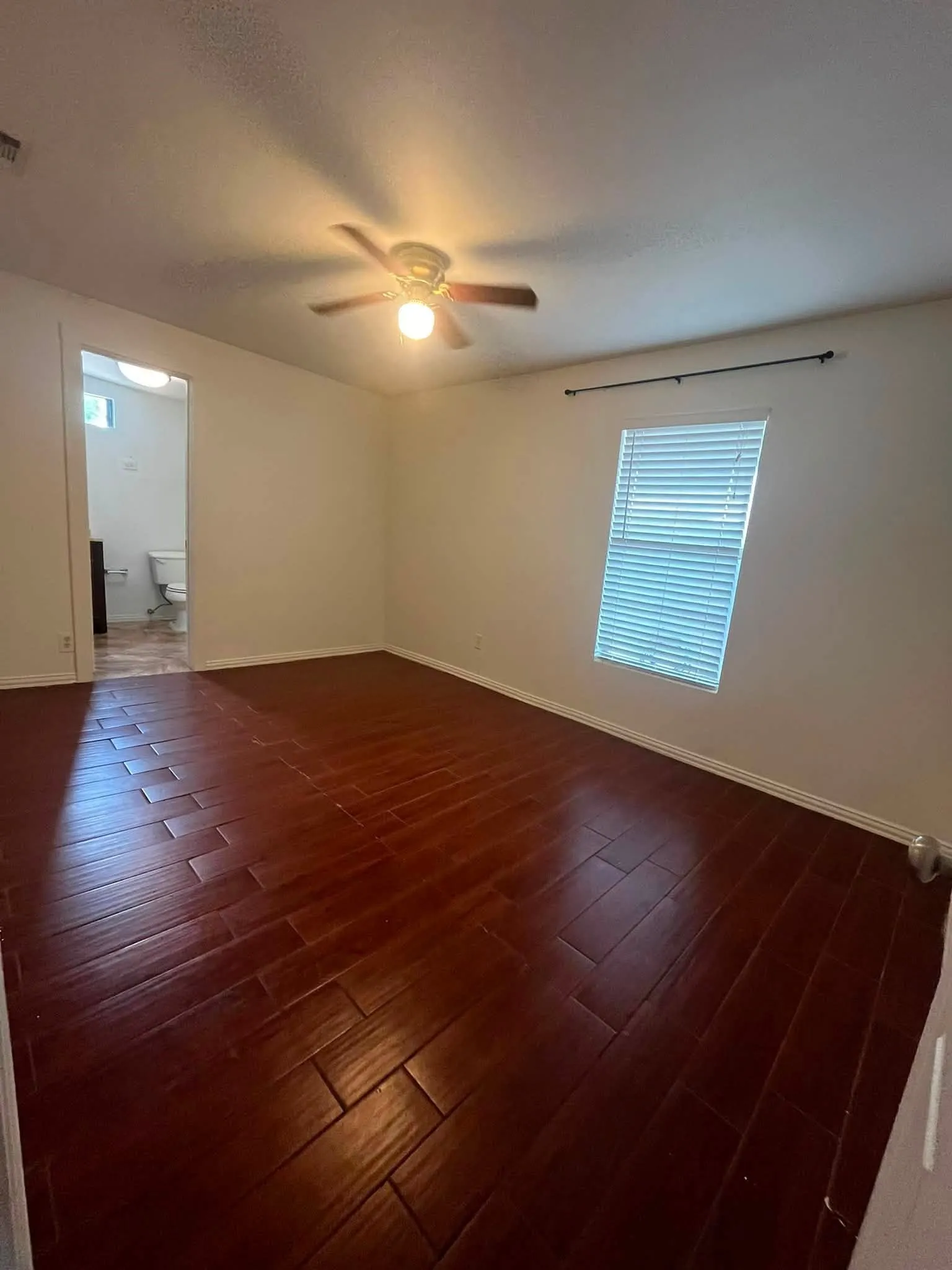 Room featuring dark wood-finish flooring, white walls, and two windows with horizontal blinds