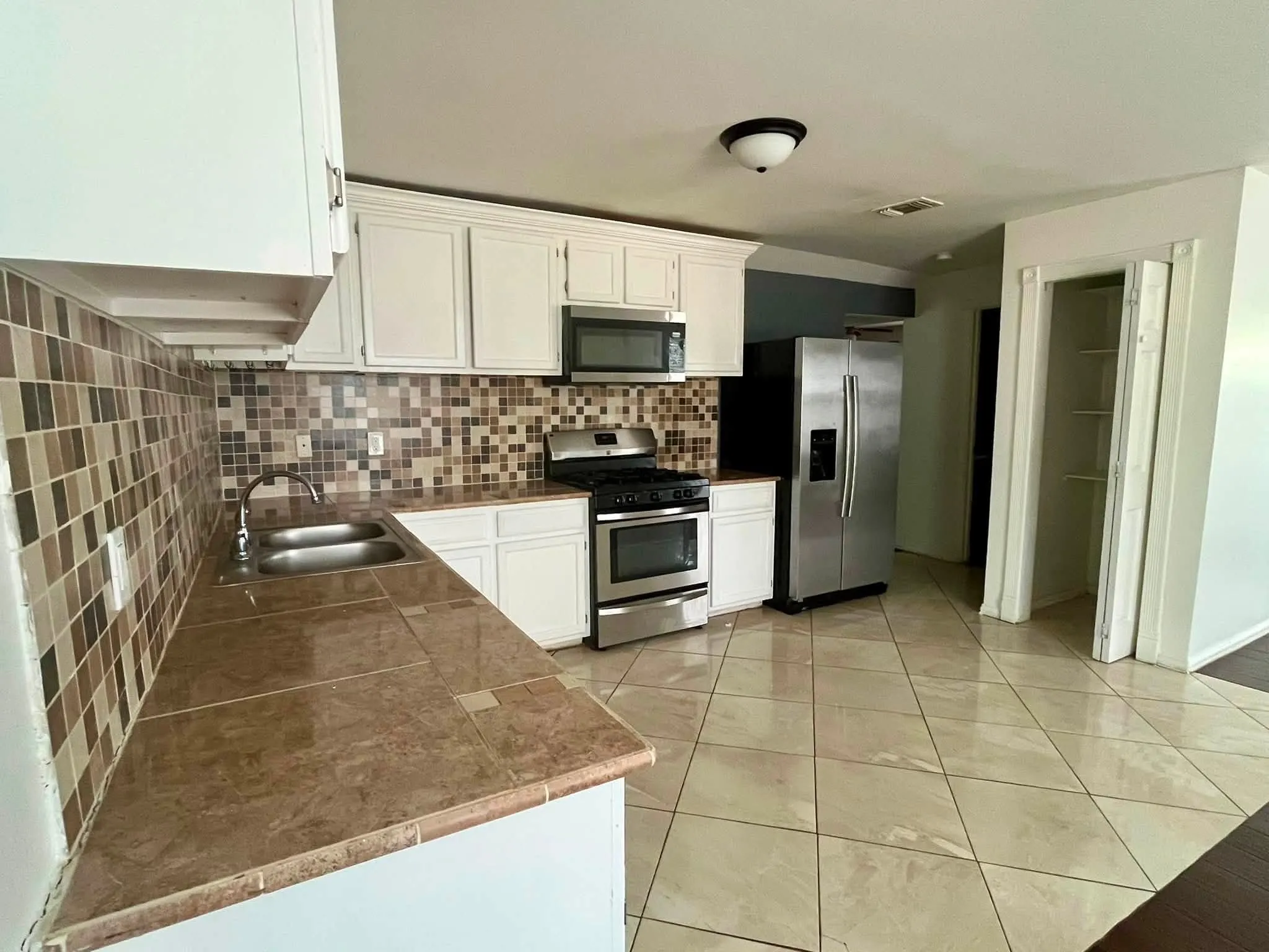 Kitchen featuring white cabinetry, stainless steel appliances, tiled countertops, mosaic tile backsplash, and light-toned floor tiling