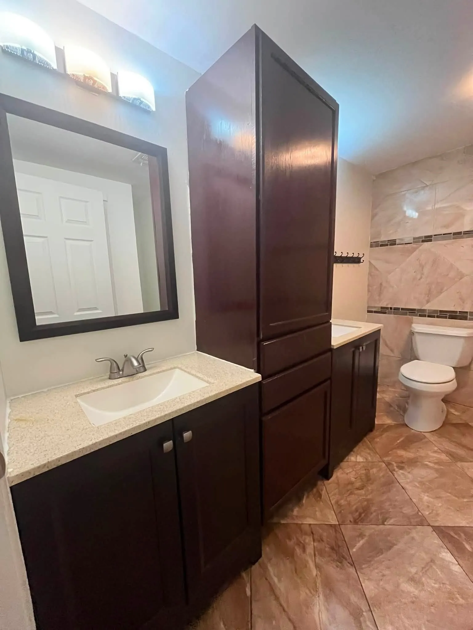Bathroom featuring a dark wood finish vanity with a light-colored countertop, an undermount sink, and a framed mirror
