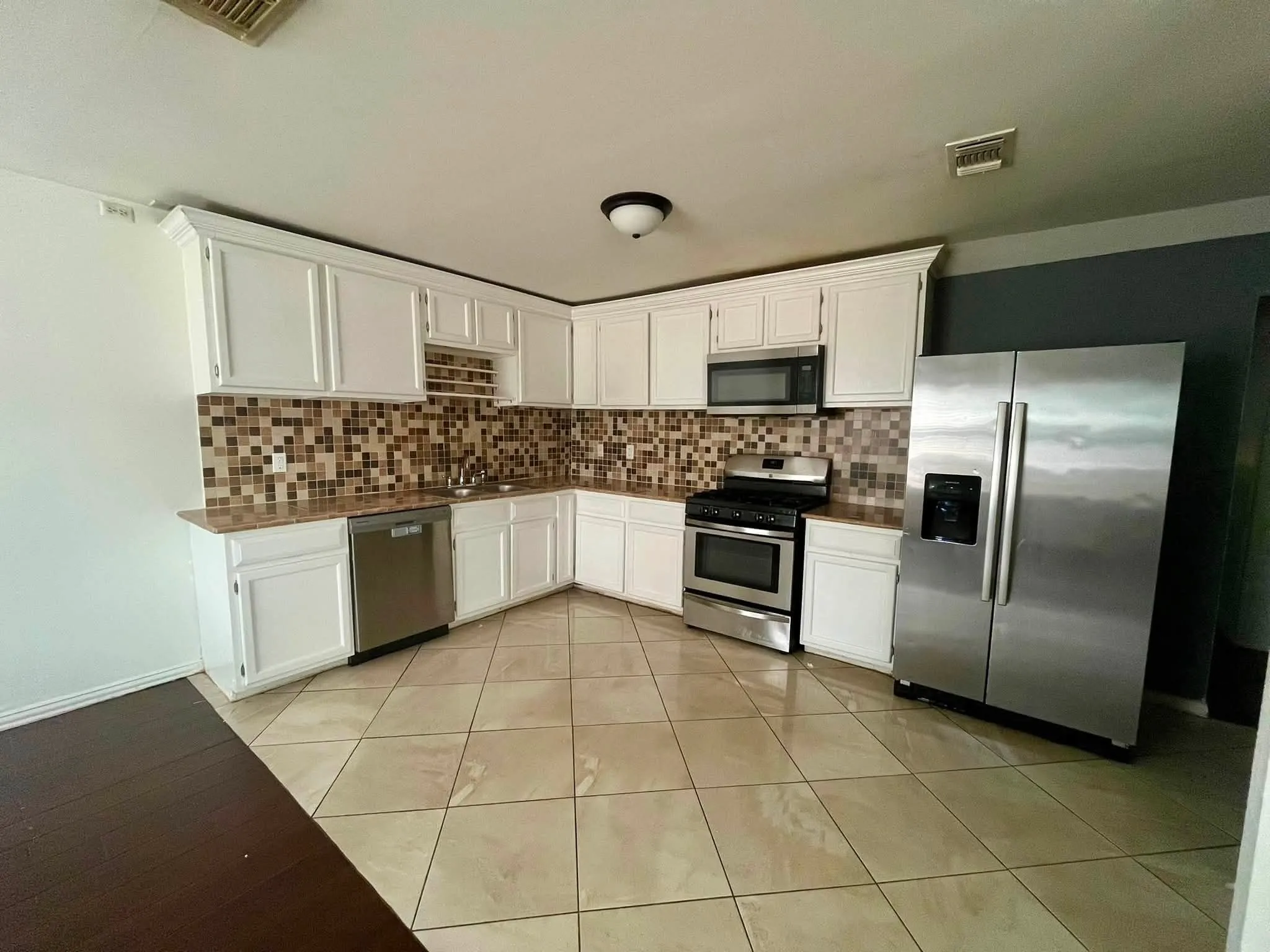 Spacious kitchen featuring white cabinetry, a mosaic tile backsplash, stainless steel appliances, a double basin sink, and large format tile flooring