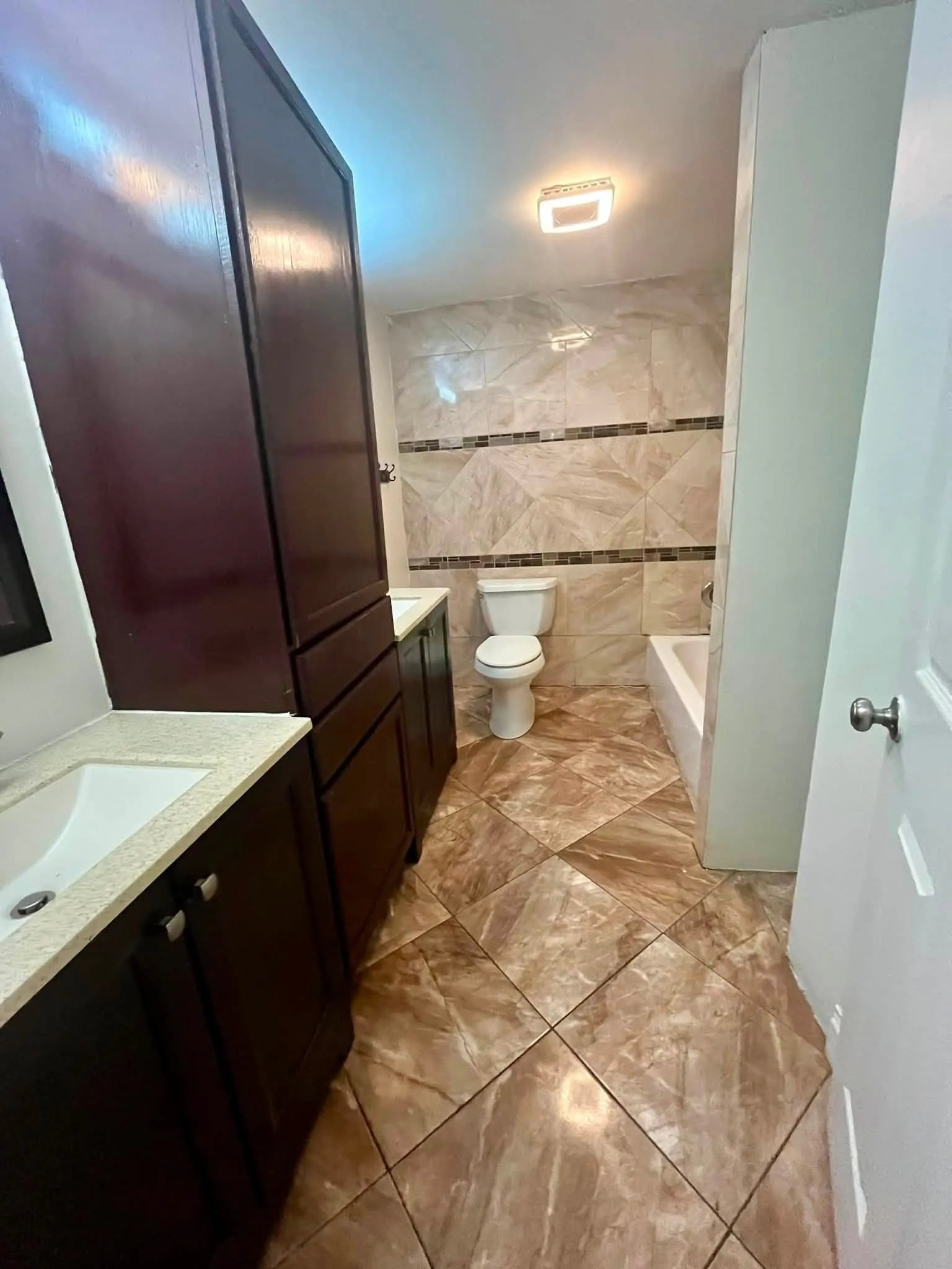 Bathroom featuring a dual vanity with dark wood cabinetry and light countertops, a built-in storage tower, a toilet, a bathtub, and patterned floor tiling