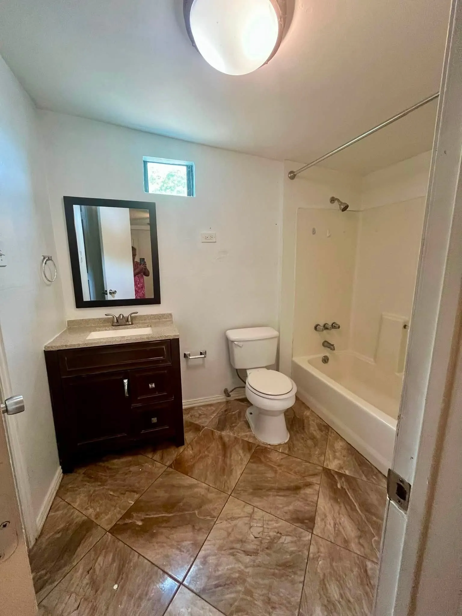 Full bathroom featuring a dark wood-finish vanity with a light-toned countertop, a rectangular undermount sink, and a framed wall mirror