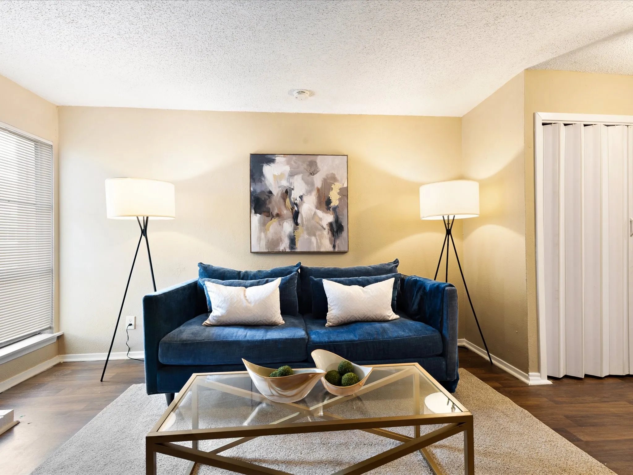 Living area featuring wood-finish flooring, a contemporary ceiling light fixture, and a window with blinds