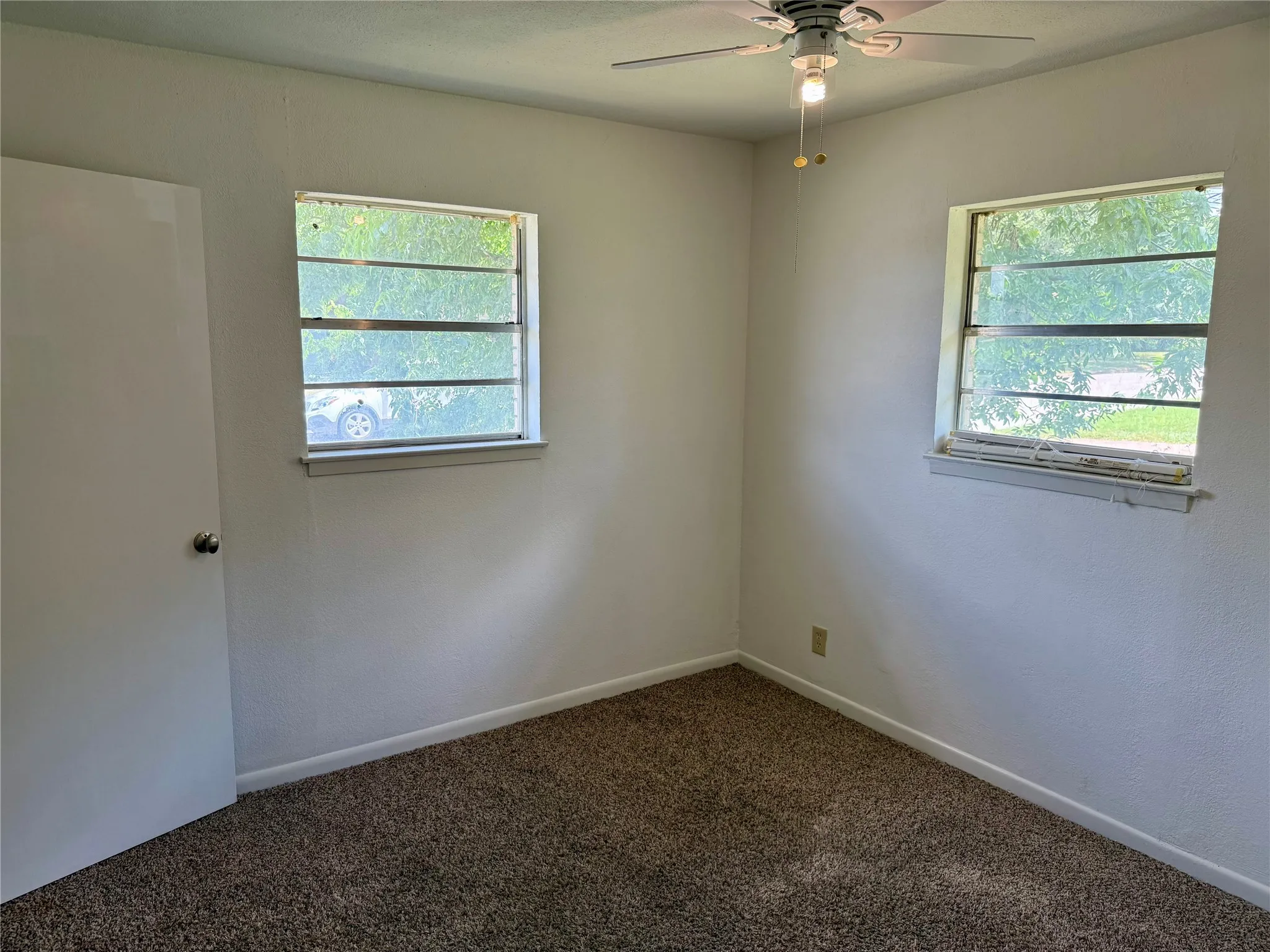 Bedroom featuring two windows, neutral wall color, ceiling fan with light fixture, white door, and carpet flooring