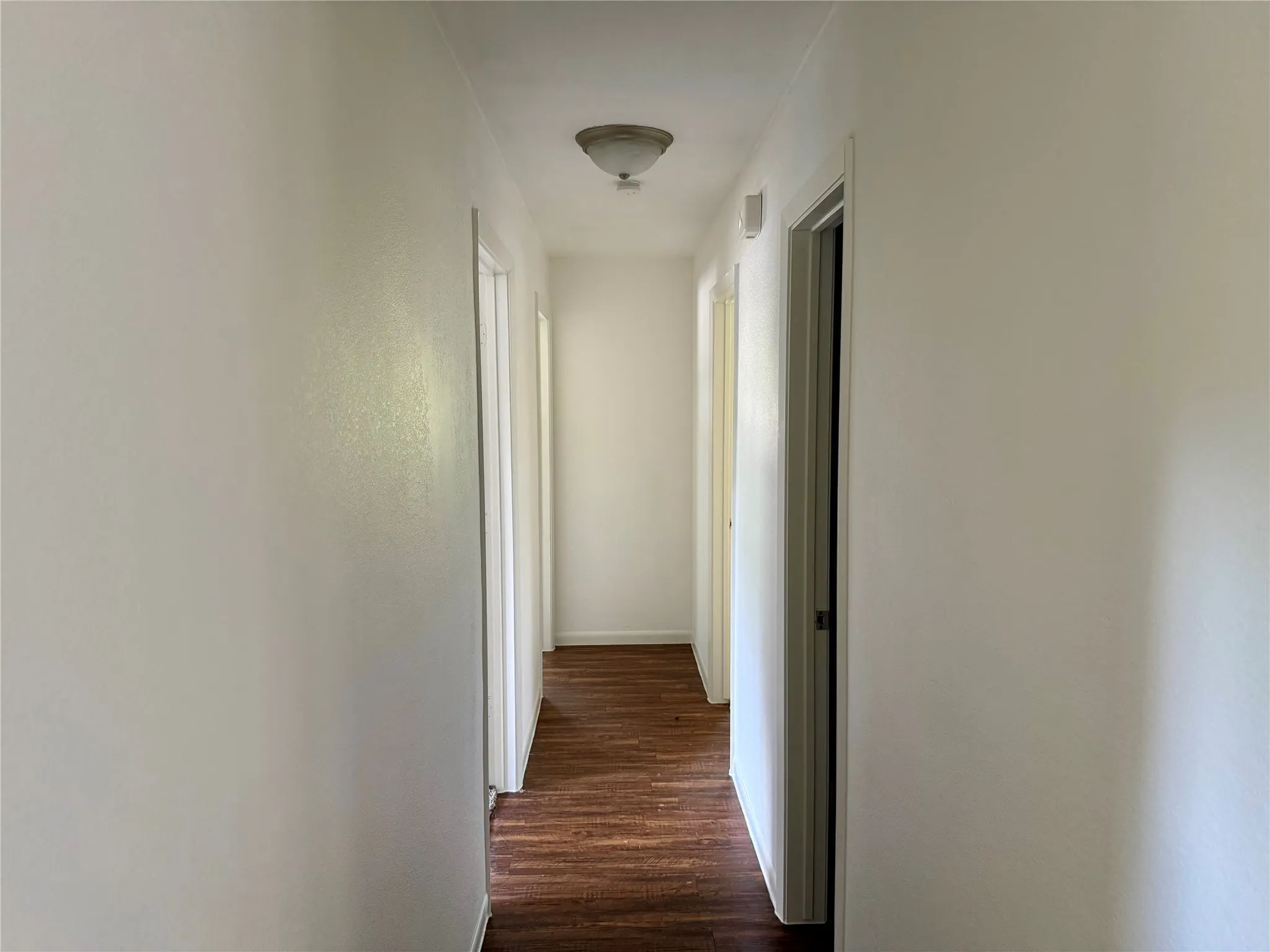 Hallway featuring wood-finish flooring, light neutral wall tones, white trim, and a ceiling-mounted light fixture