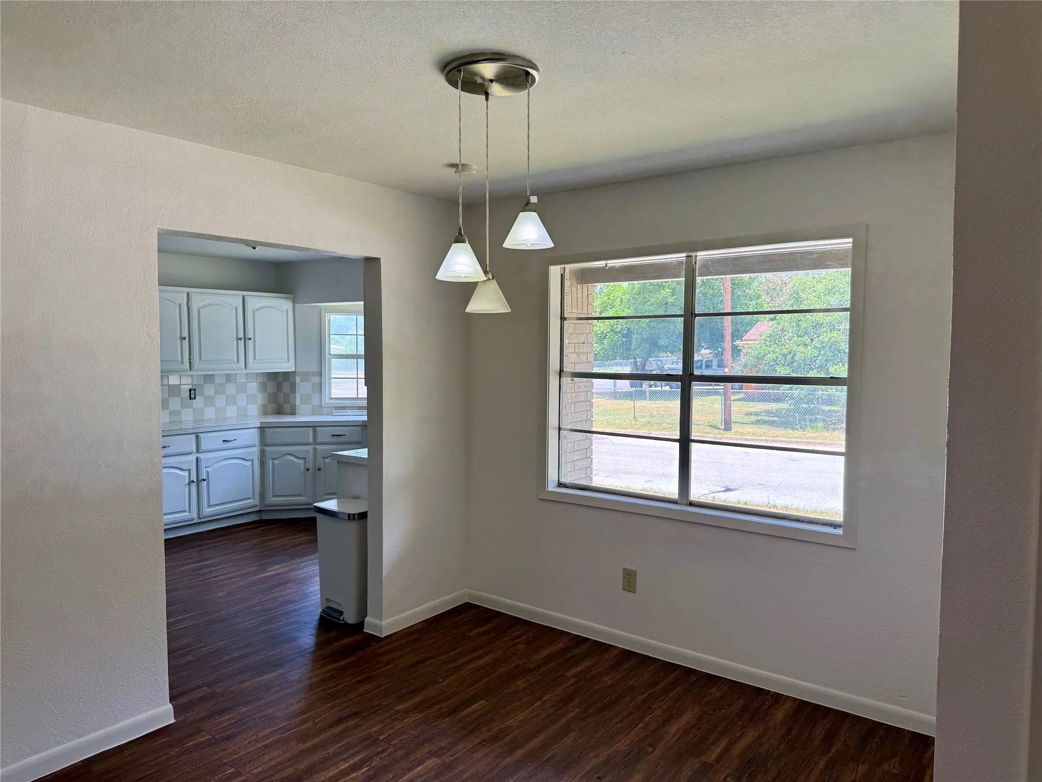 Room featuring wood-finish flooring, a contemporary pendant light fixture, and a large window with horizontal muntins