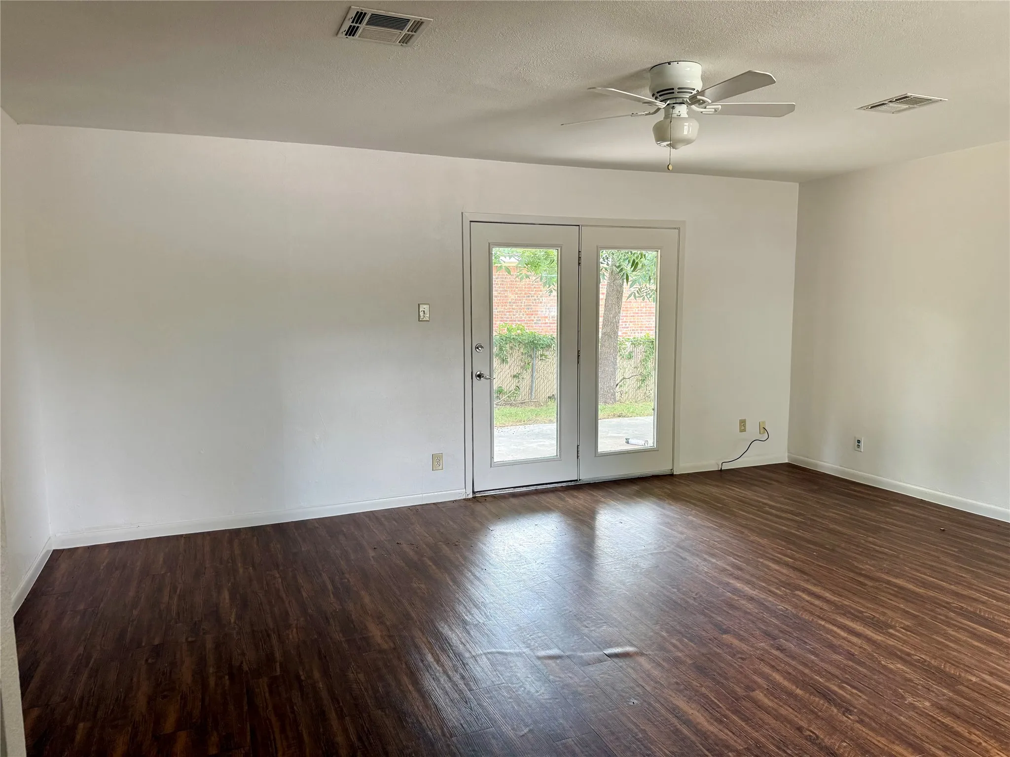 Bright room featuring dark wood-finish flooring and a contemporary ceiling fan