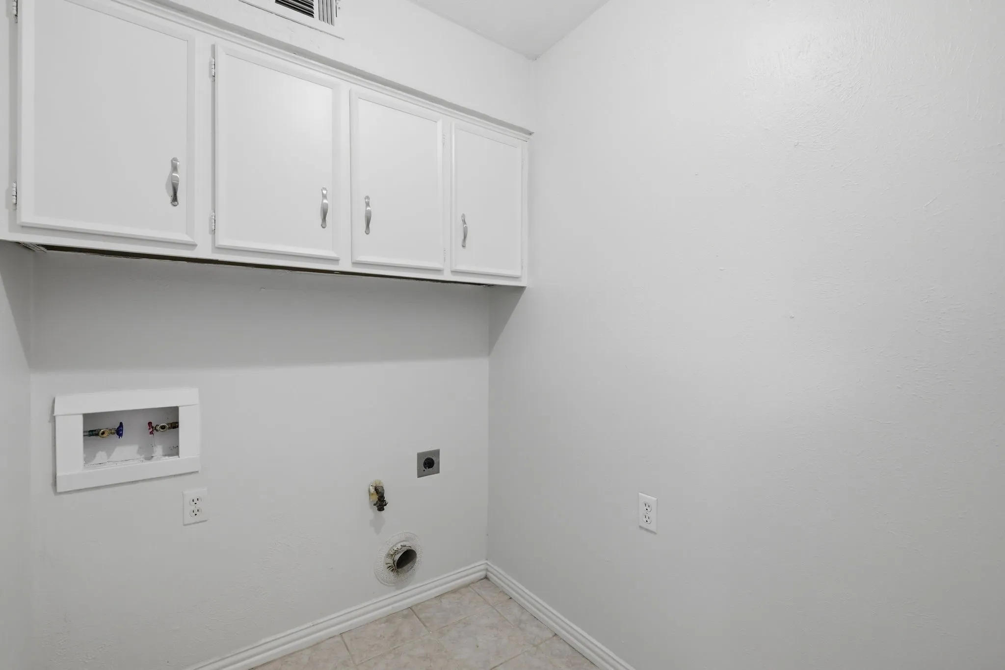 Dedicated utility area featuring white cabinetry, tile flooring, and wall-mounted plumbing connections