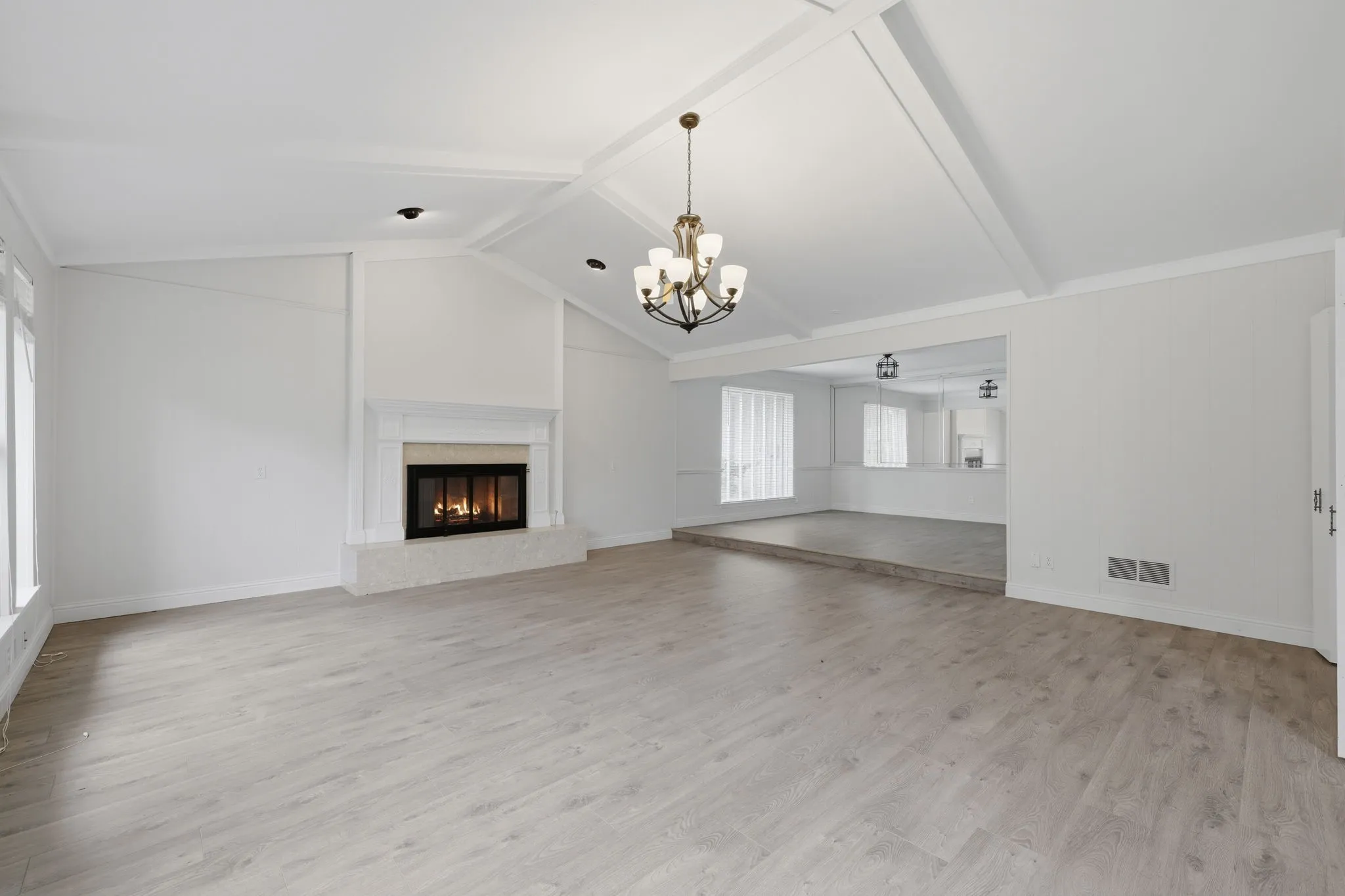 Vaulted ceiling with exposed beams, wood-finish flooring, and a fireplace with a white mantel and stone hearth