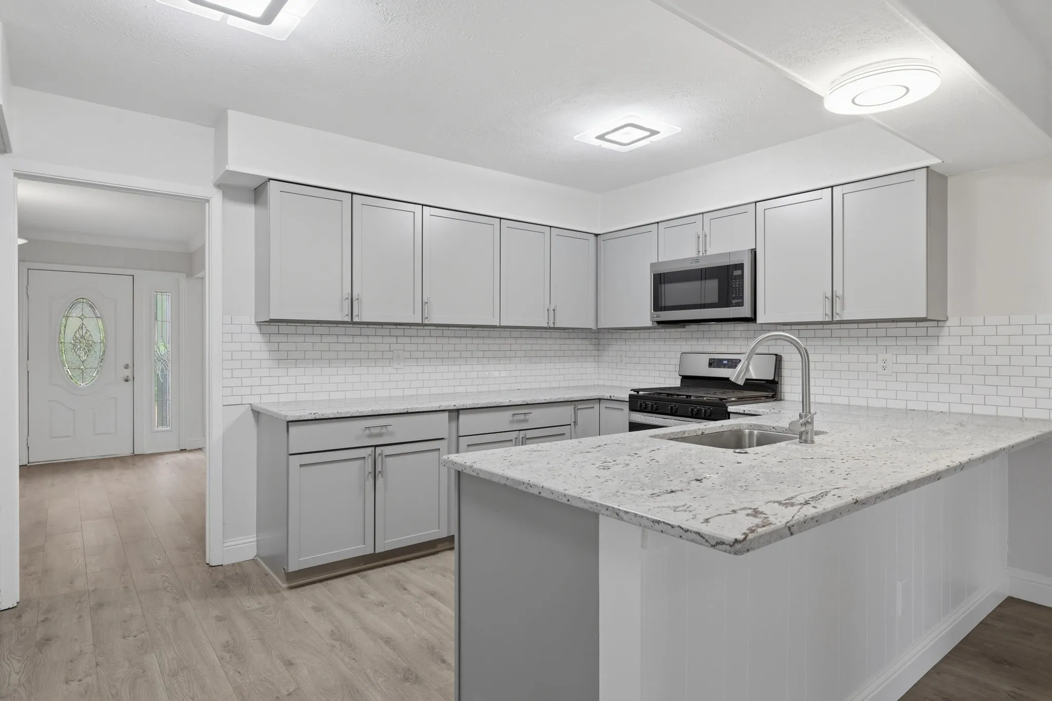 Modern kitchen featuring light gray cabinetry, white subway tile backsplash, stainless steel appliances, granite countertops, and wood-finish flooring