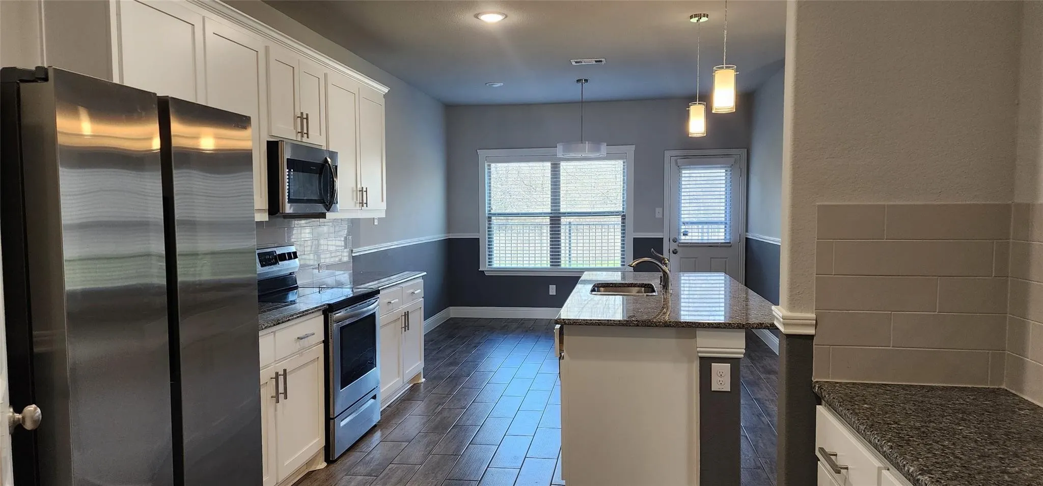 Contemporary kitchen featuring white cabinetry, stainless steel appliances, granite countertops, and wood-finish tile flooring