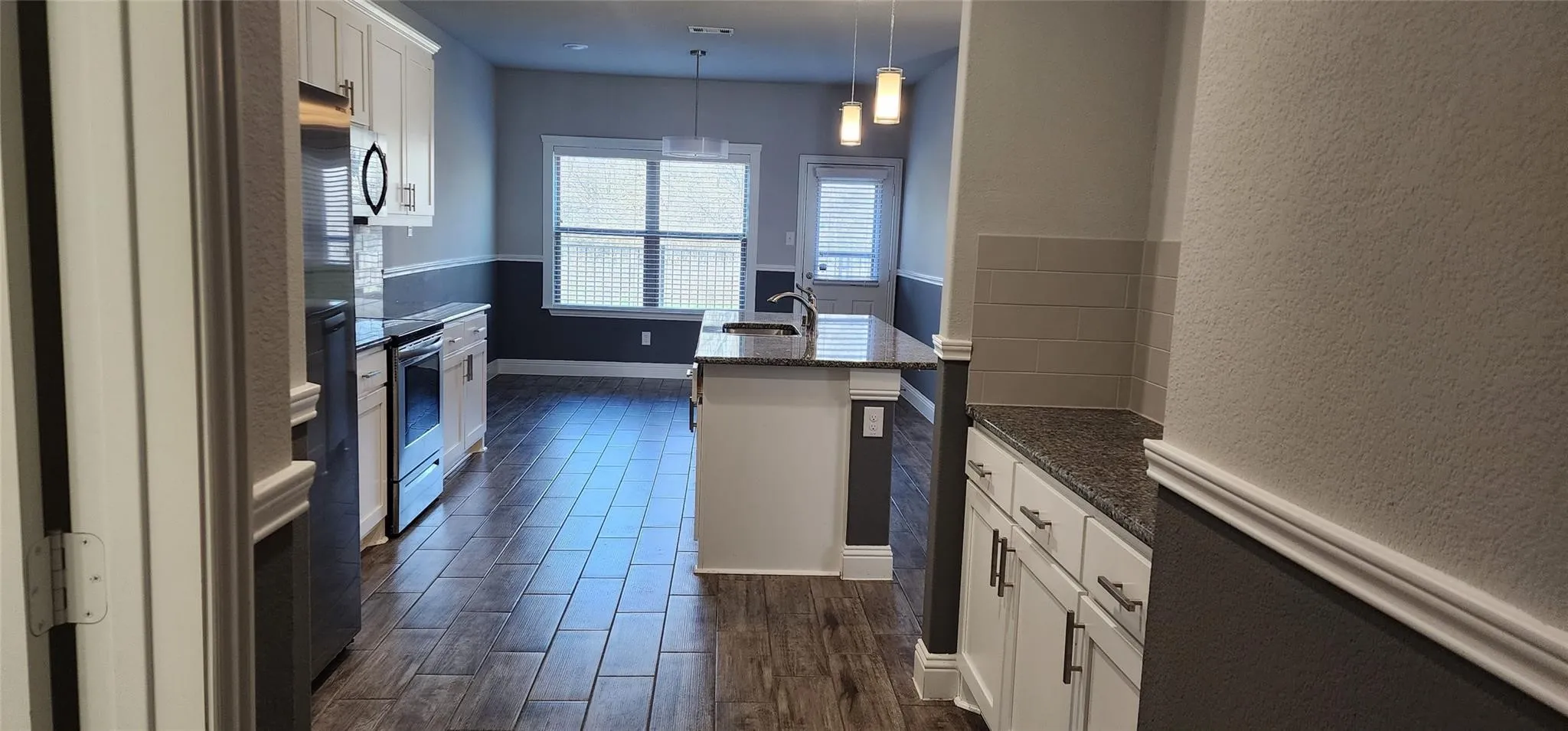 Kitchen featuring white cabinetry, stainless steel appliances, a center island with sink, pendant lighting, and wood-finish flooring