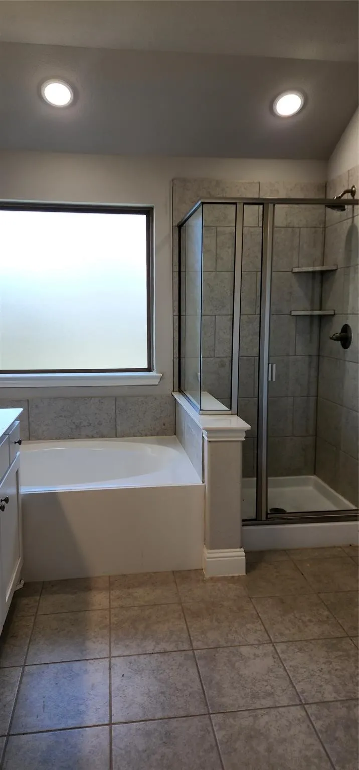 Bathroom featuring a built-in tub, tiled shower with glass enclosure, recessed lighting, privacy window, and tiled flooring