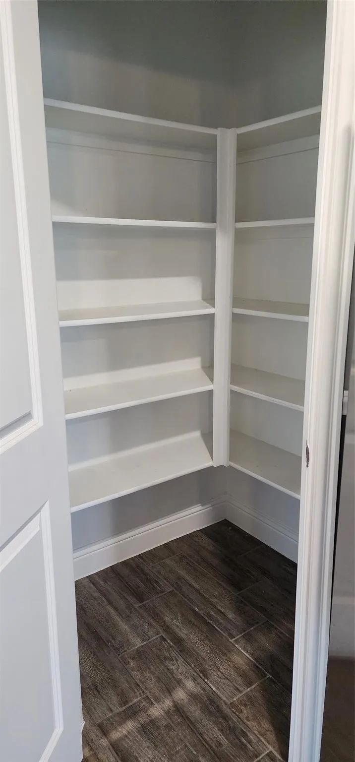 Walk-in pantry featuring white shelving, wood-finish tile flooring, and white baseboards
