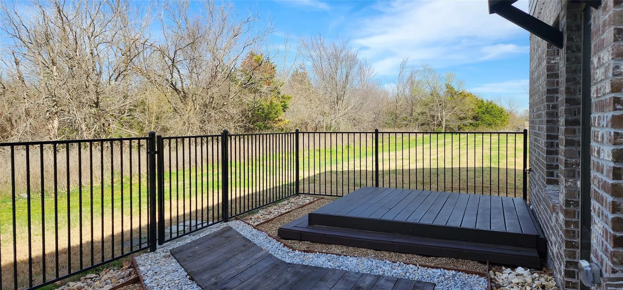 Exterior patio featuring a two-tier composite deck, bordered by decorative gravel and a black metal fence