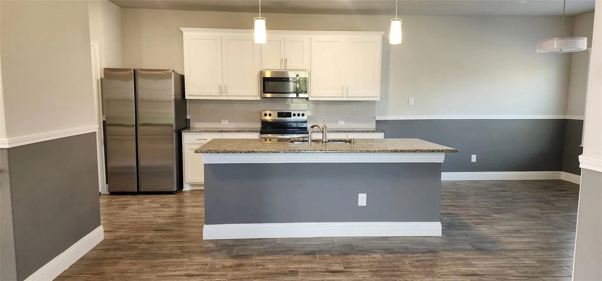 Open-concept kitchen featuring an island with a light-colored countertop, white cabinetry, stainless steel appliances, and wood-finish flooring