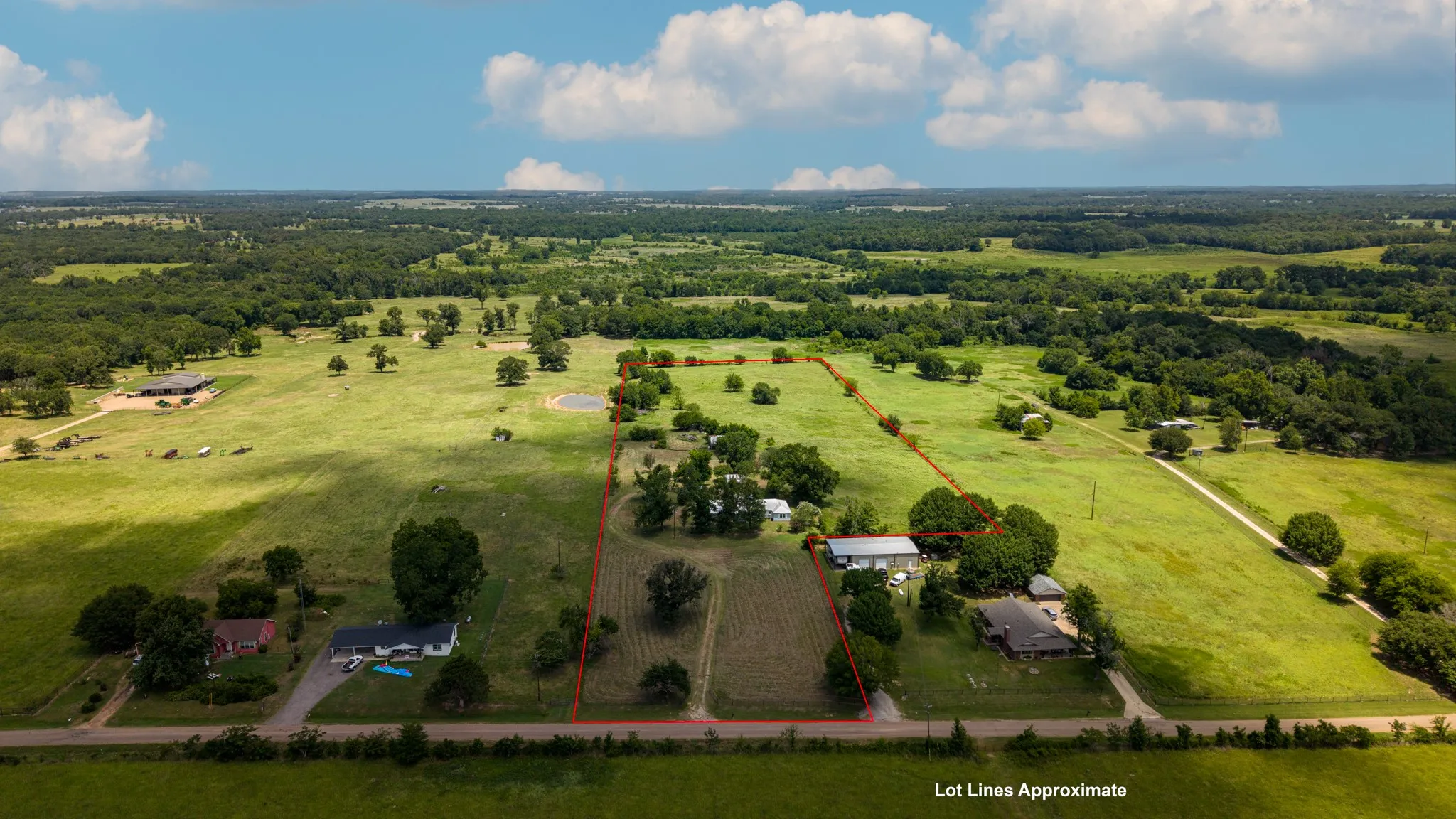Expansive rural landscape featuring a single-story residence, multiple outbuildings, and a pond