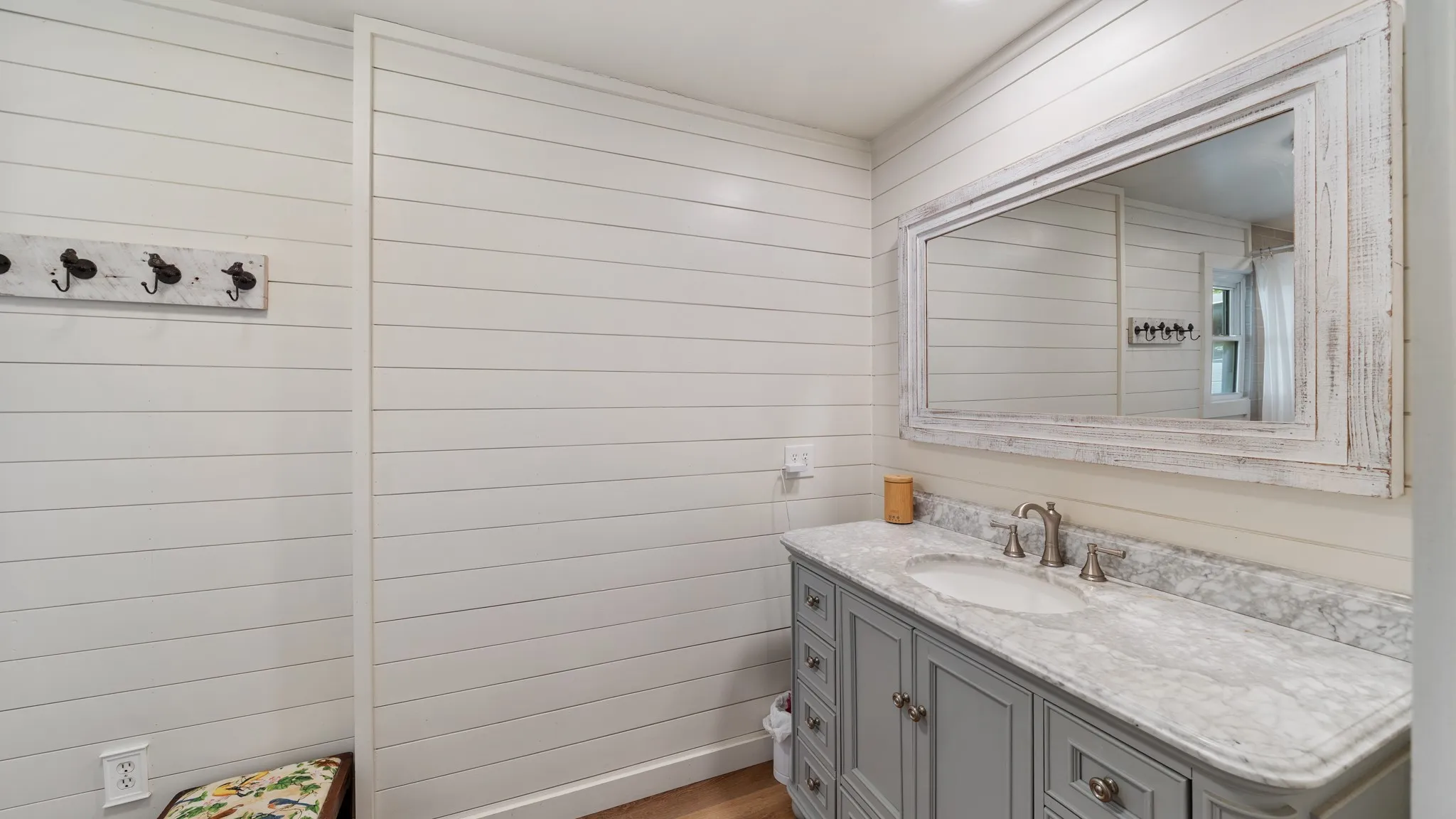 Shiplap walls complement a vanity featuring a light gray cabinet, a white oval undermount sink, a marble countertop, and a distressed wood-frame mirror
