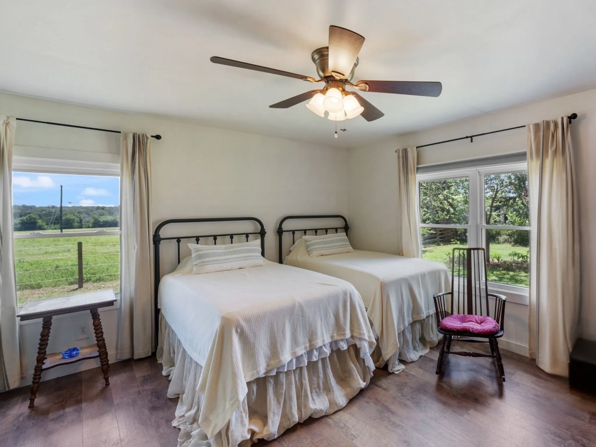 Spacious room featuring wood-finish flooring, two large windows, a ceiling fan with light fixture, and white walls