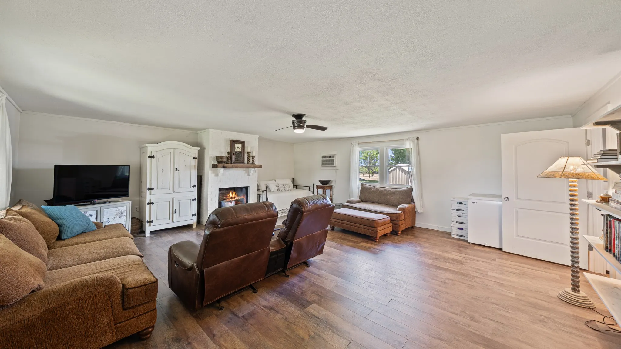 Spacious living area featuring wood-finish flooring, a white-painted fireplace with a wood mantle, and a ceiling fan