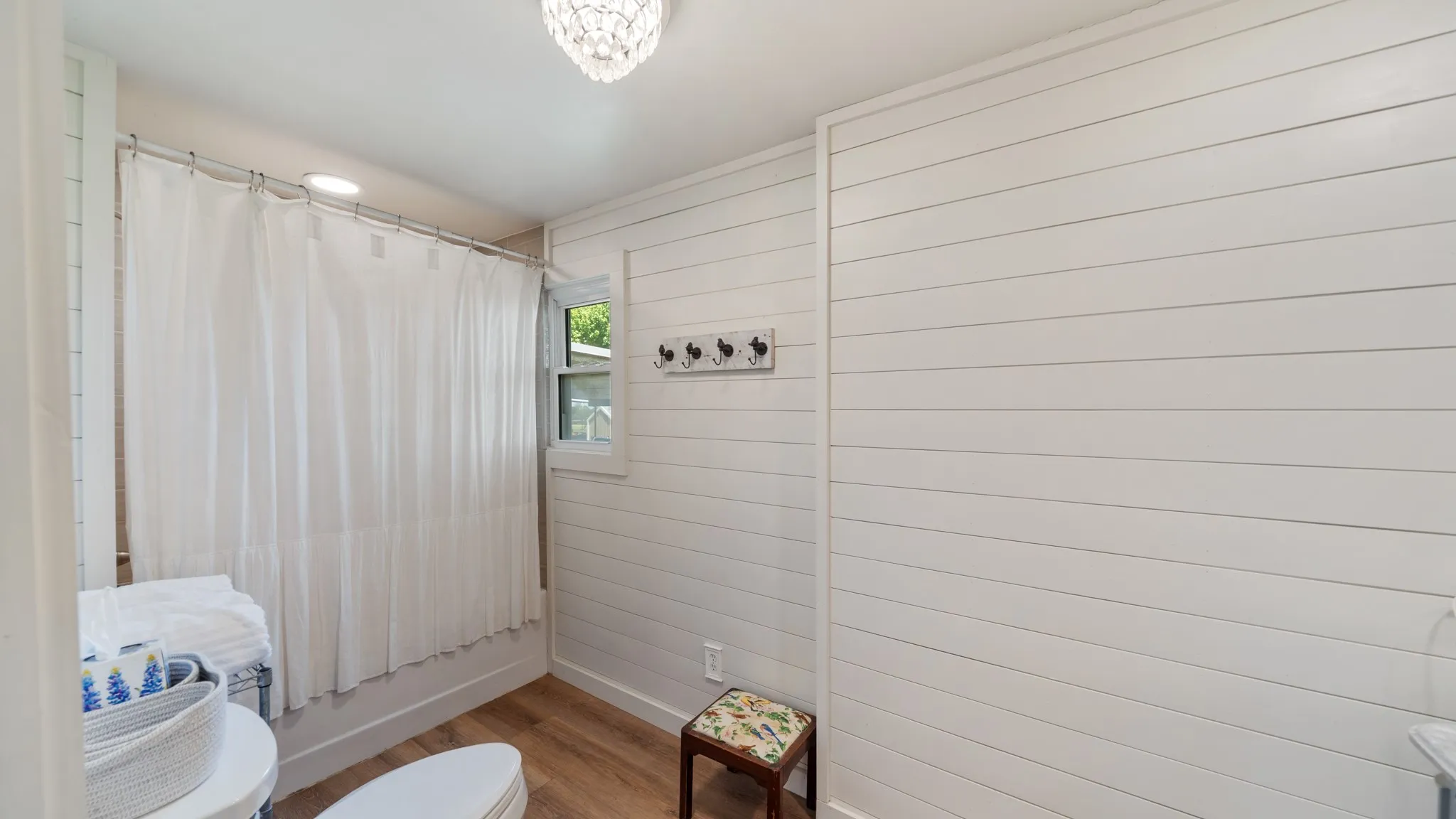 Bathroom featuring white shiplap walls, wood-finish flooring, a window, and a built-in shower with a curtain rod