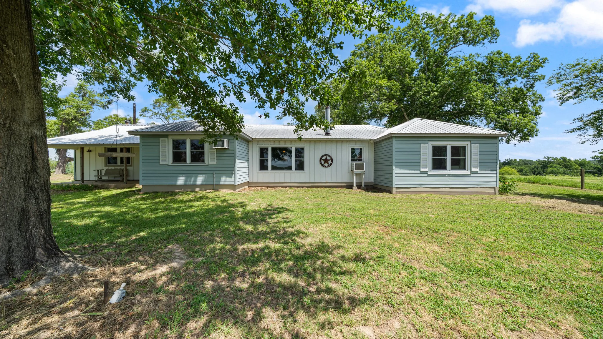 Ranch-style exterior with light blue and white siding, featuring a covered porch and multiple windows with white shutters