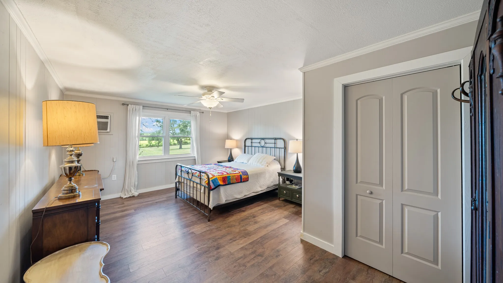 Spacious room featuring wood-finish flooring, a ceiling fan, and a large window with white trim