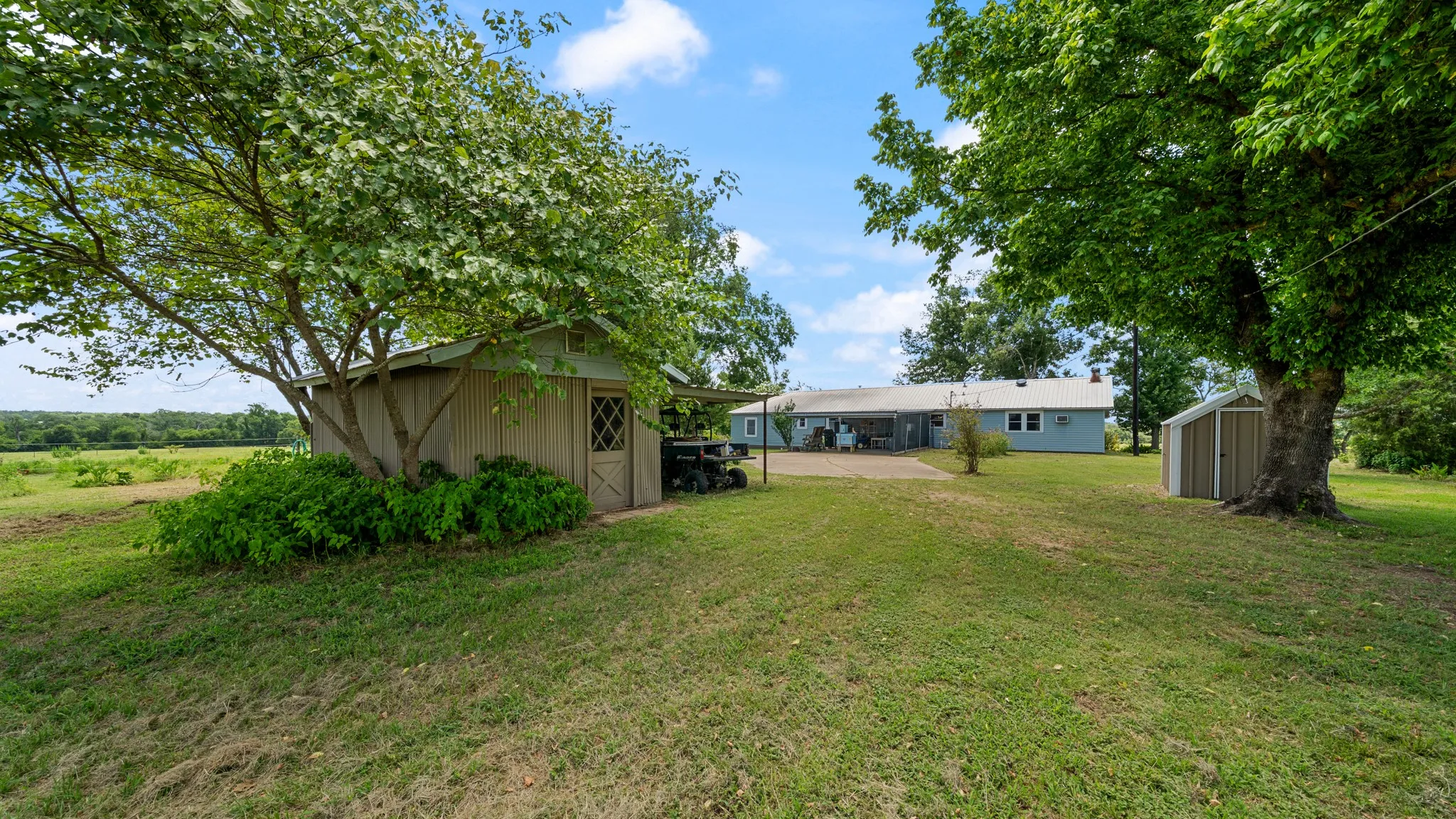Expansive green lawn featuring mature trees, a detached storage shed with a diamond-pane window, and a secondary metal storage shed