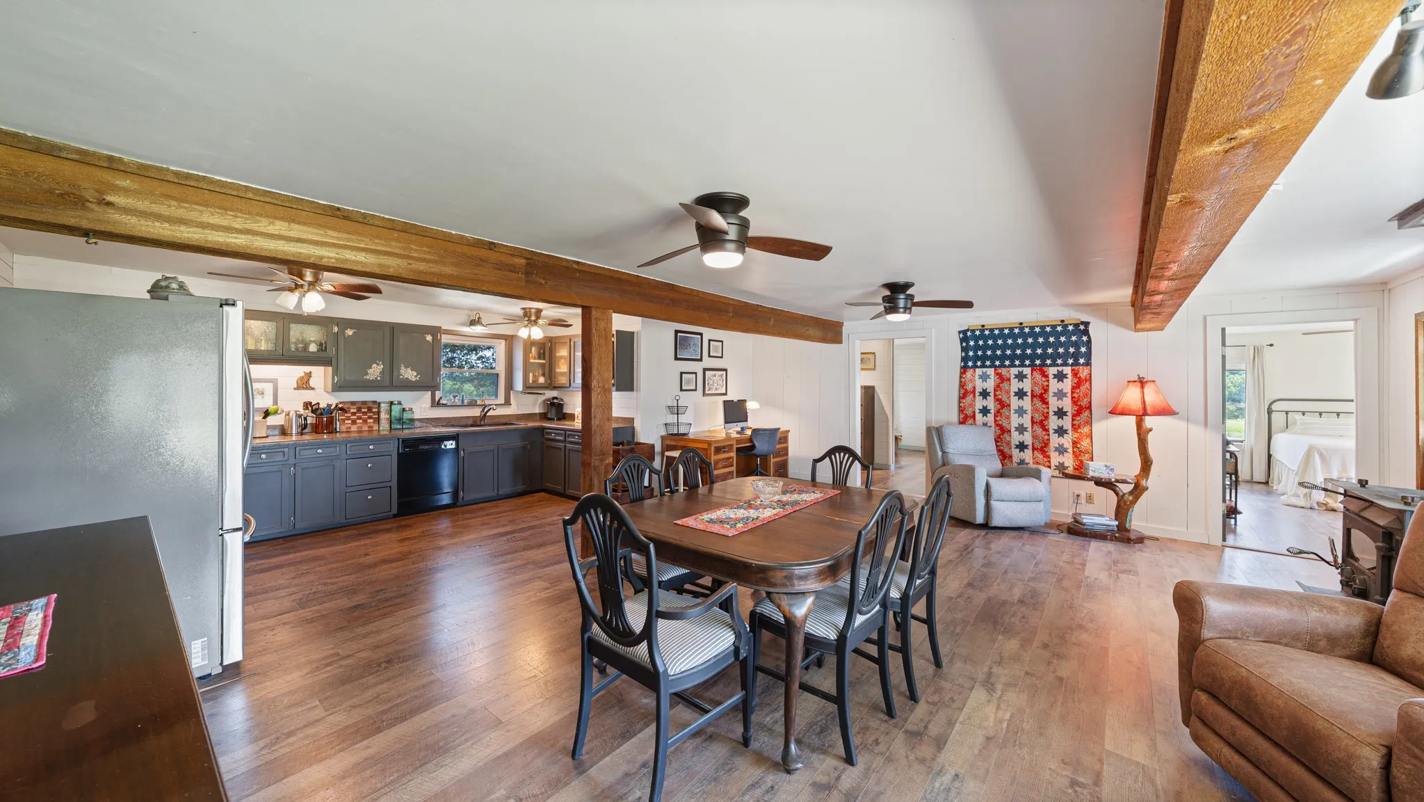 Open-concept living area featuring wood-finish flooring, exposed wood beams, and white paneled walls