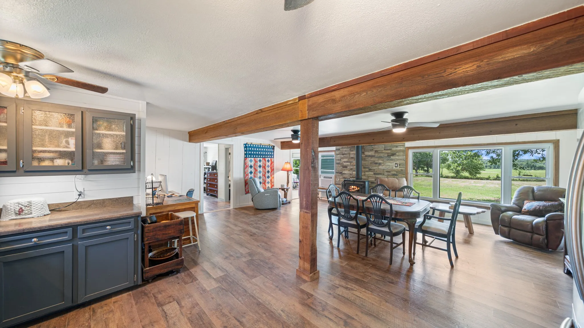 Open-concept interior featuring wood-finish flooring, exposed wood beams, and a stone-clad wall with a built-in stove