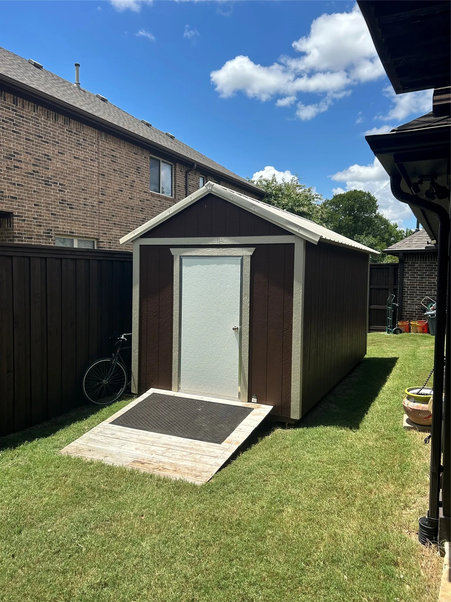 Detached storage shed with brown siding and white trim, featuring a white door, a sloped wood ramp, and a metal roof