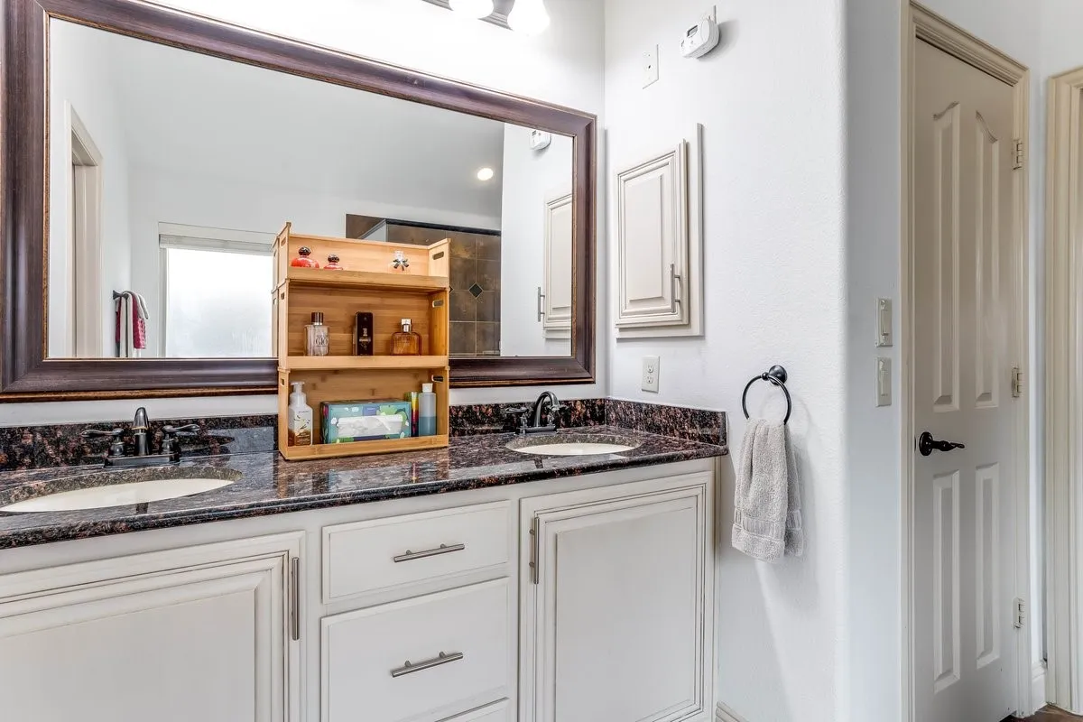 Double vanity with under-mount sinks, dark stone countertop, and custom white cabinetry