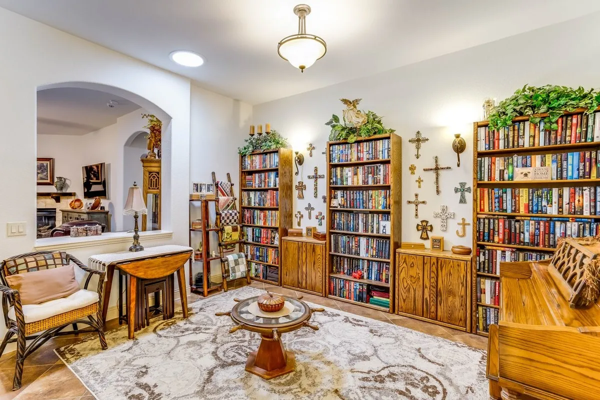 Dedicated room featuring two expansive built-in bookshelves with lower storage cabinetry, an arched entryway, recessed lighting, and a prominent ceiling light fixture