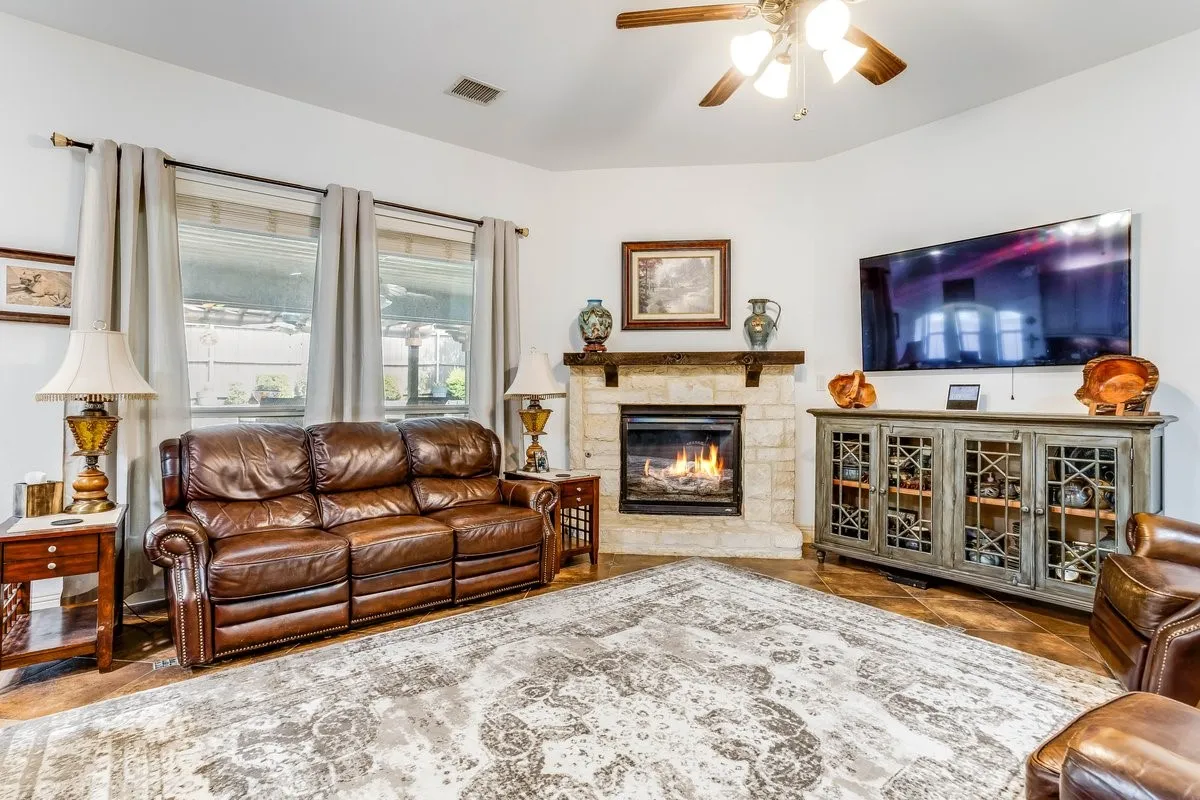 Living area featuring tile flooring, a stone-faced fireplace with a wood mantle, and a ceiling fan with integrated lighting