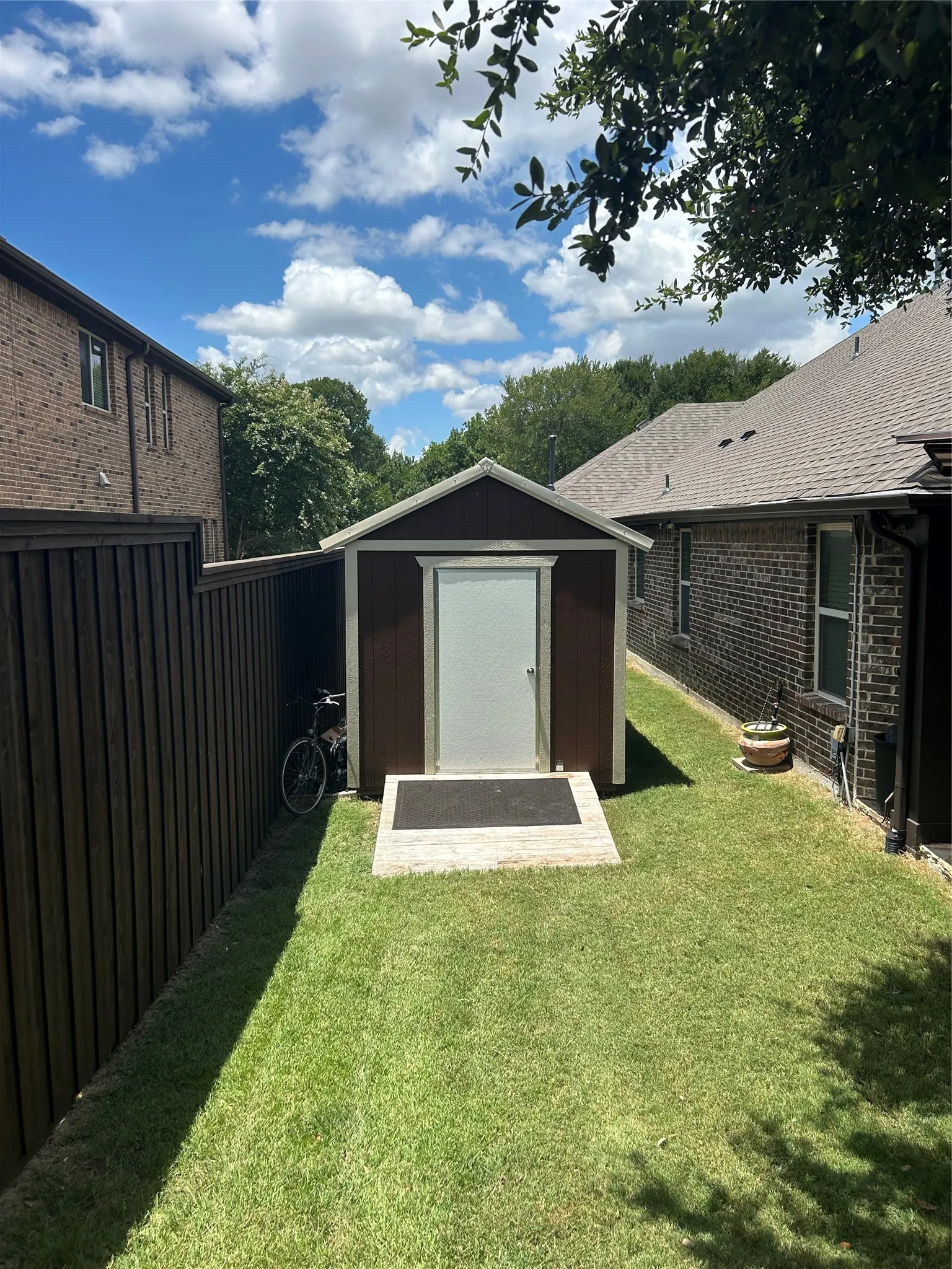 Backyard storage shed with a light-colored door, dark siding, and a gabled roof