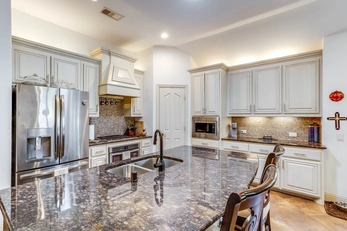 Kitchen featuring an expansive island with a dual-basin sink, under-cabinet lighting, stainless steel appliances, a decorative range hood, and light-toned cabinetry