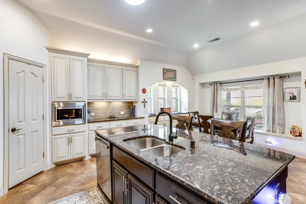 Kitchen featuring a large island with a double basin sink, granite countertops, light wood-finish cabinetry, and stainless steel appliances