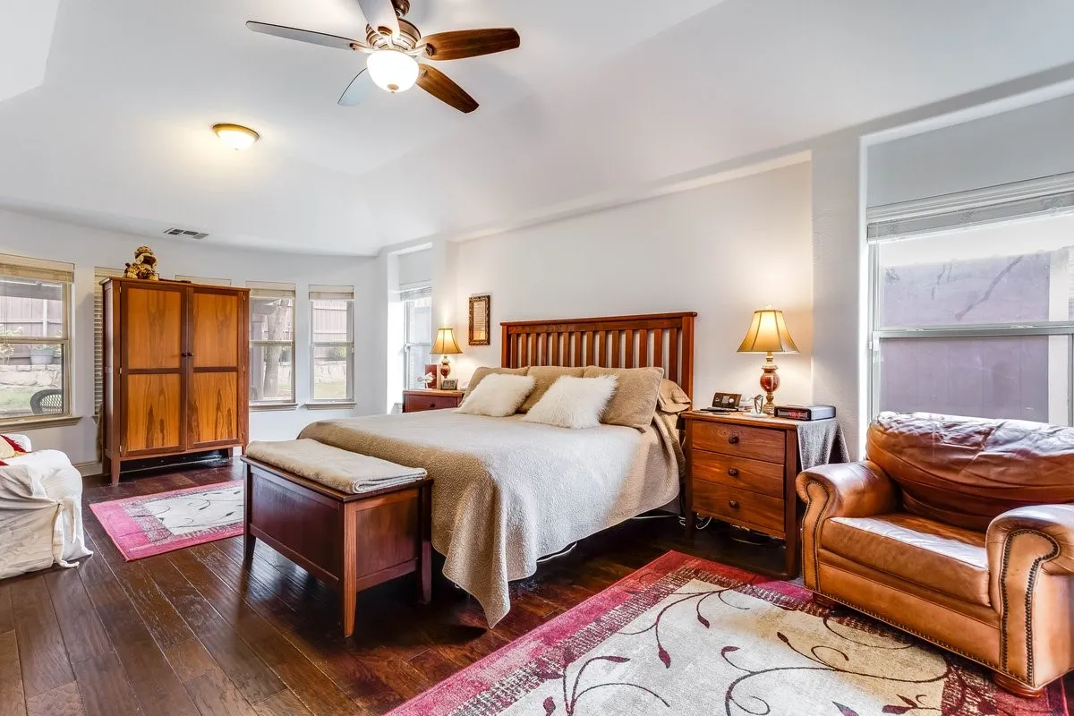 Spacious room featuring vaulted ceilings, wood-finish flooring, multiple windows, and a ceiling fan